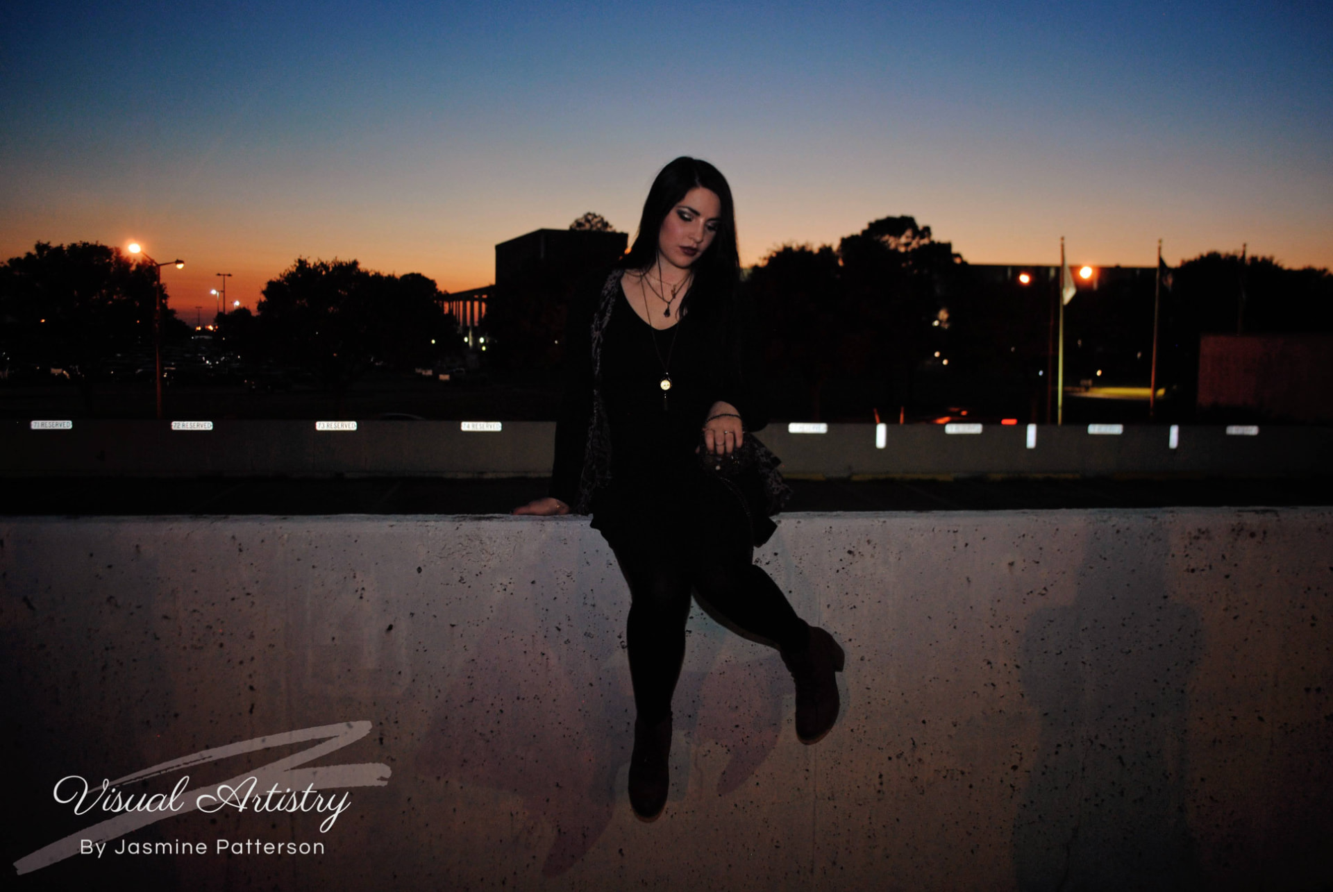 Woman in black seated on a concrete ledge against a sunset sky
