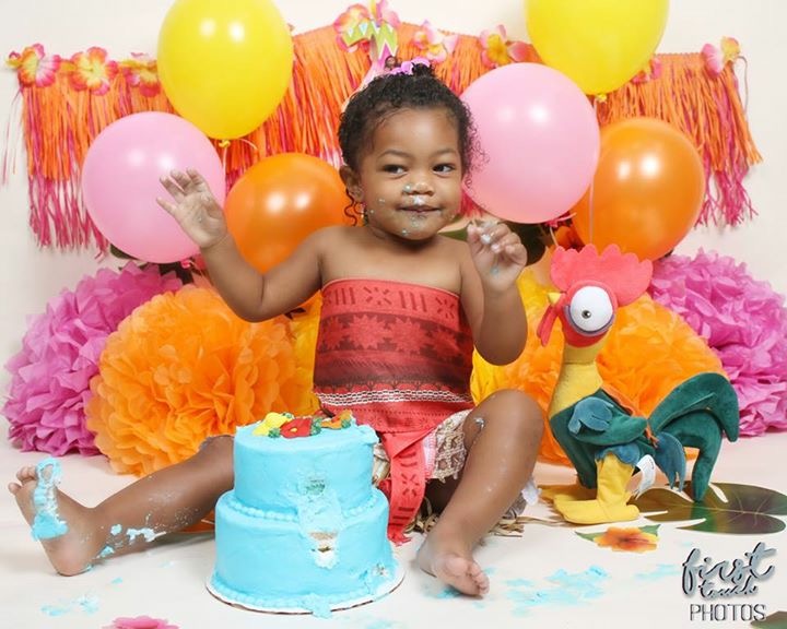 Toddler at a luau-themed cake smash surrounded by balloons and paper flowers