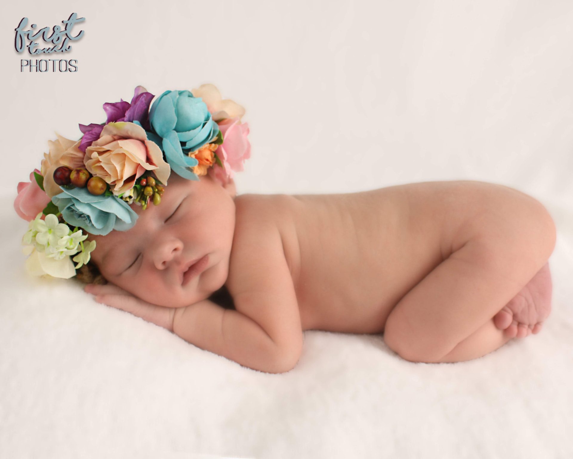 Sleeping newborn wearing a large pastel flower crown on a white blanket