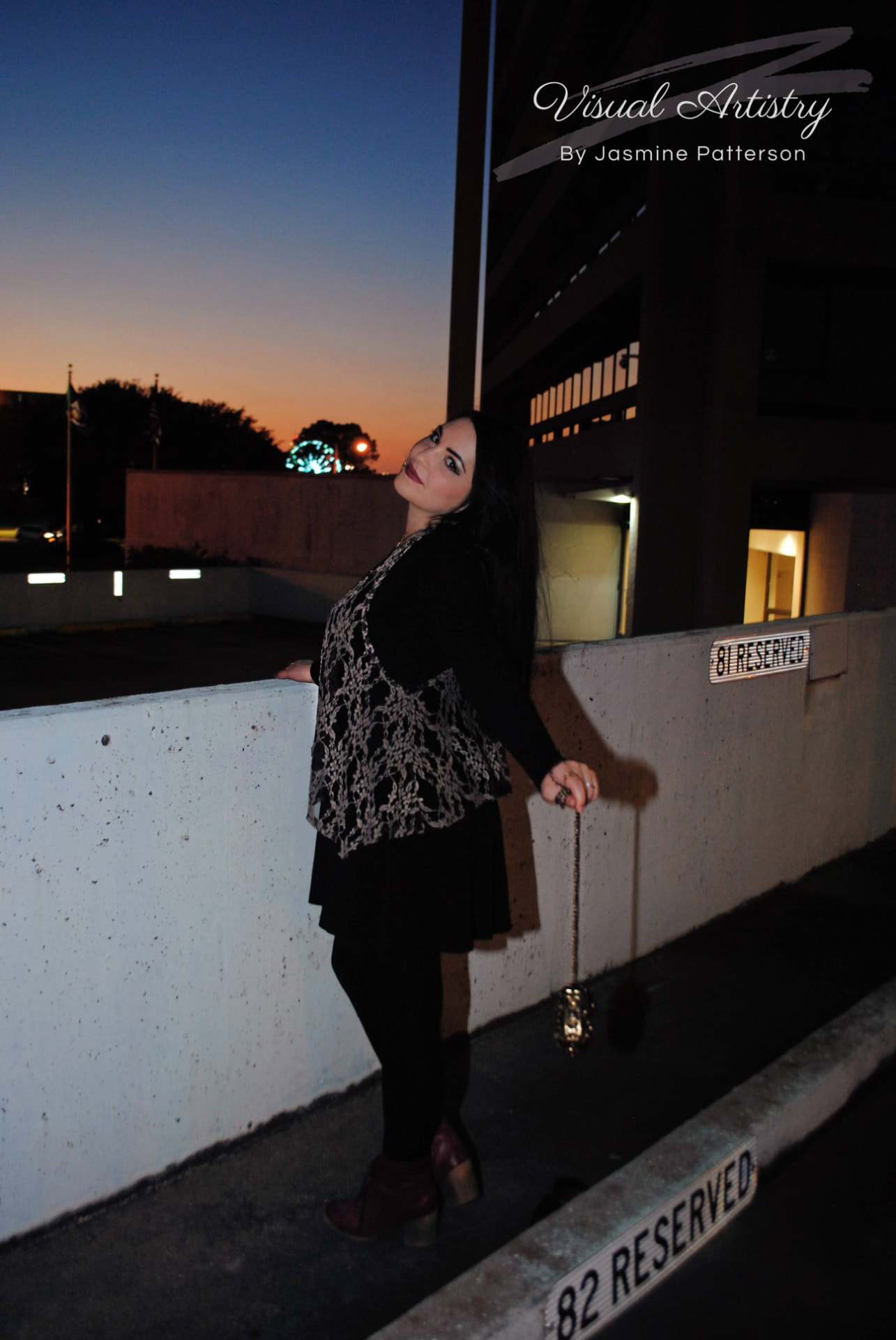Woman in black and lace leaning on a concrete ledge at dusk, city lights behind