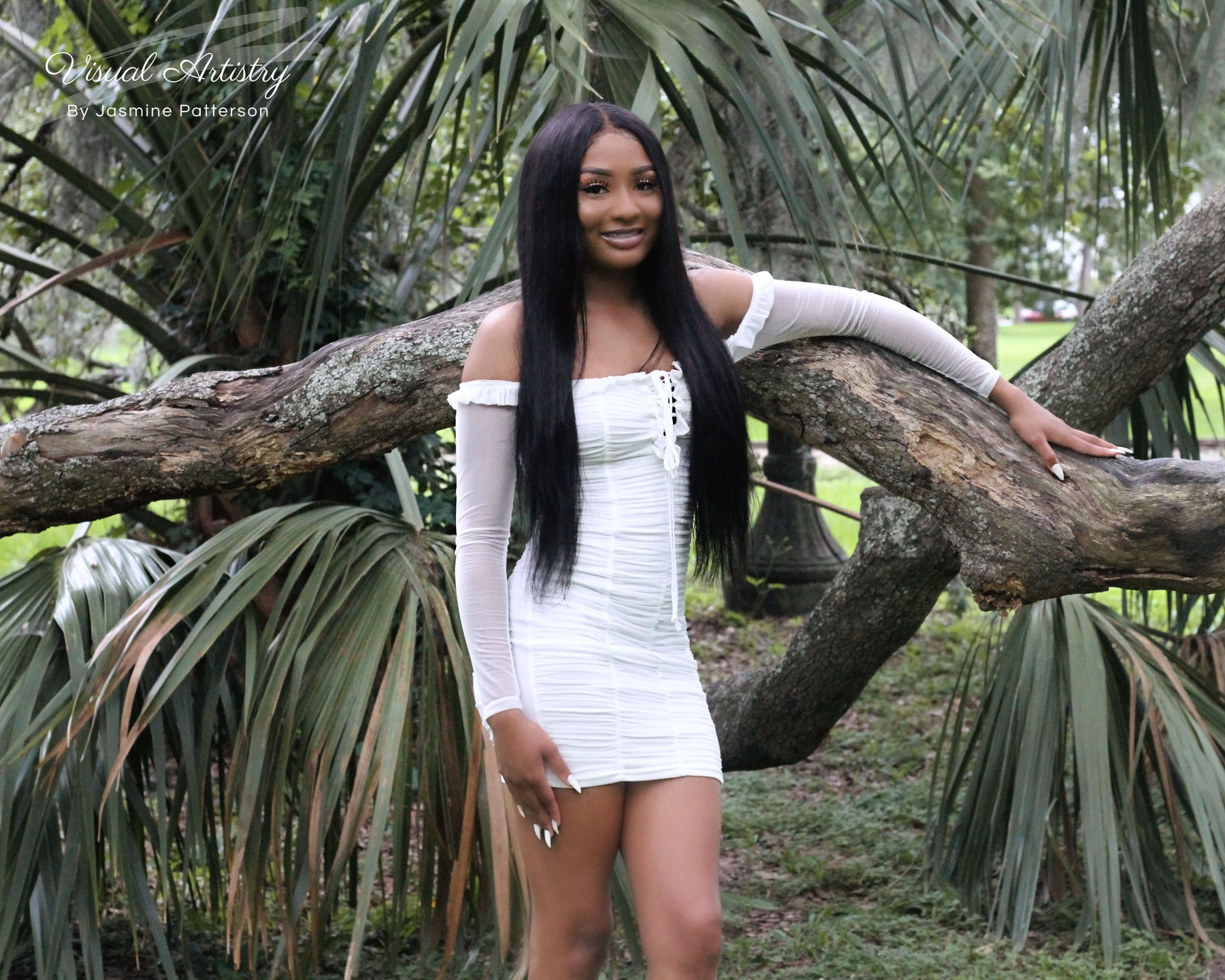 Young woman in a white dress leaning on a palm tree