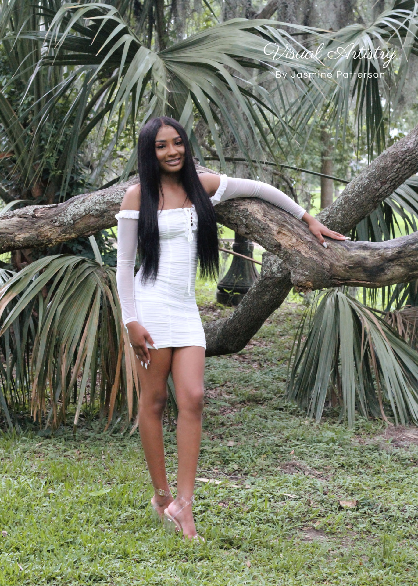 Graduate in a white dress leaning against a tree