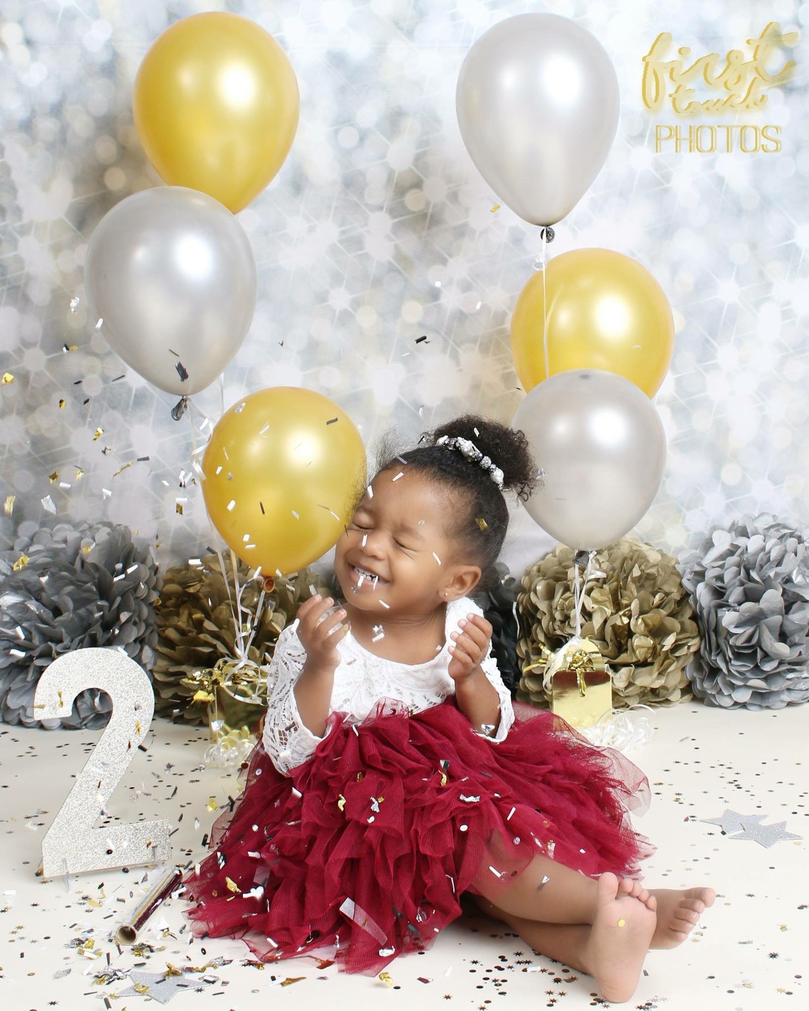Toddler in a burgundy tutu celebrating with gold and silver balloons