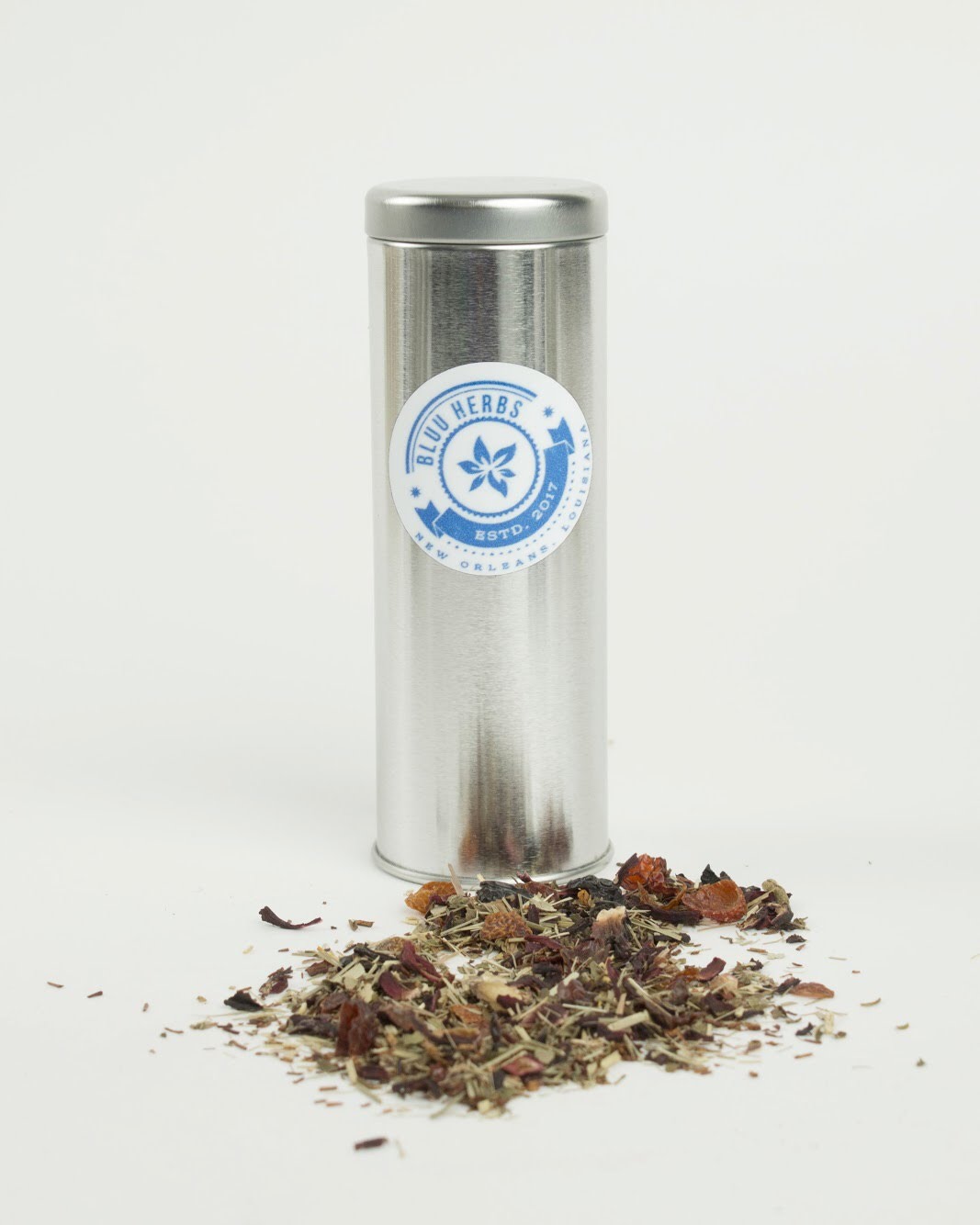 Tall silver Bluu Herbs tea tin with loose herbal tea spilled at its base