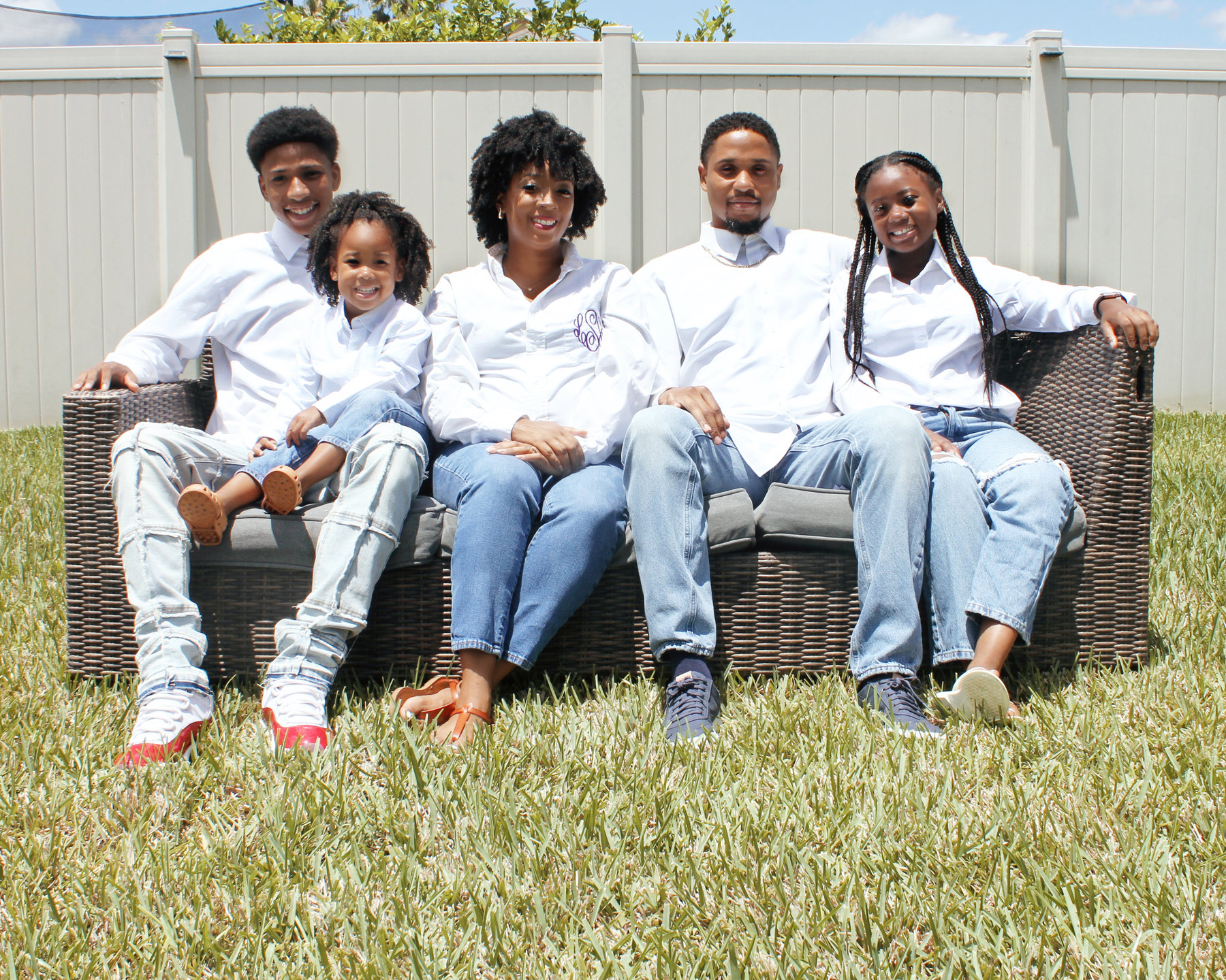 Family of five in matching white shirts and jeans seated on an outdoor sofa