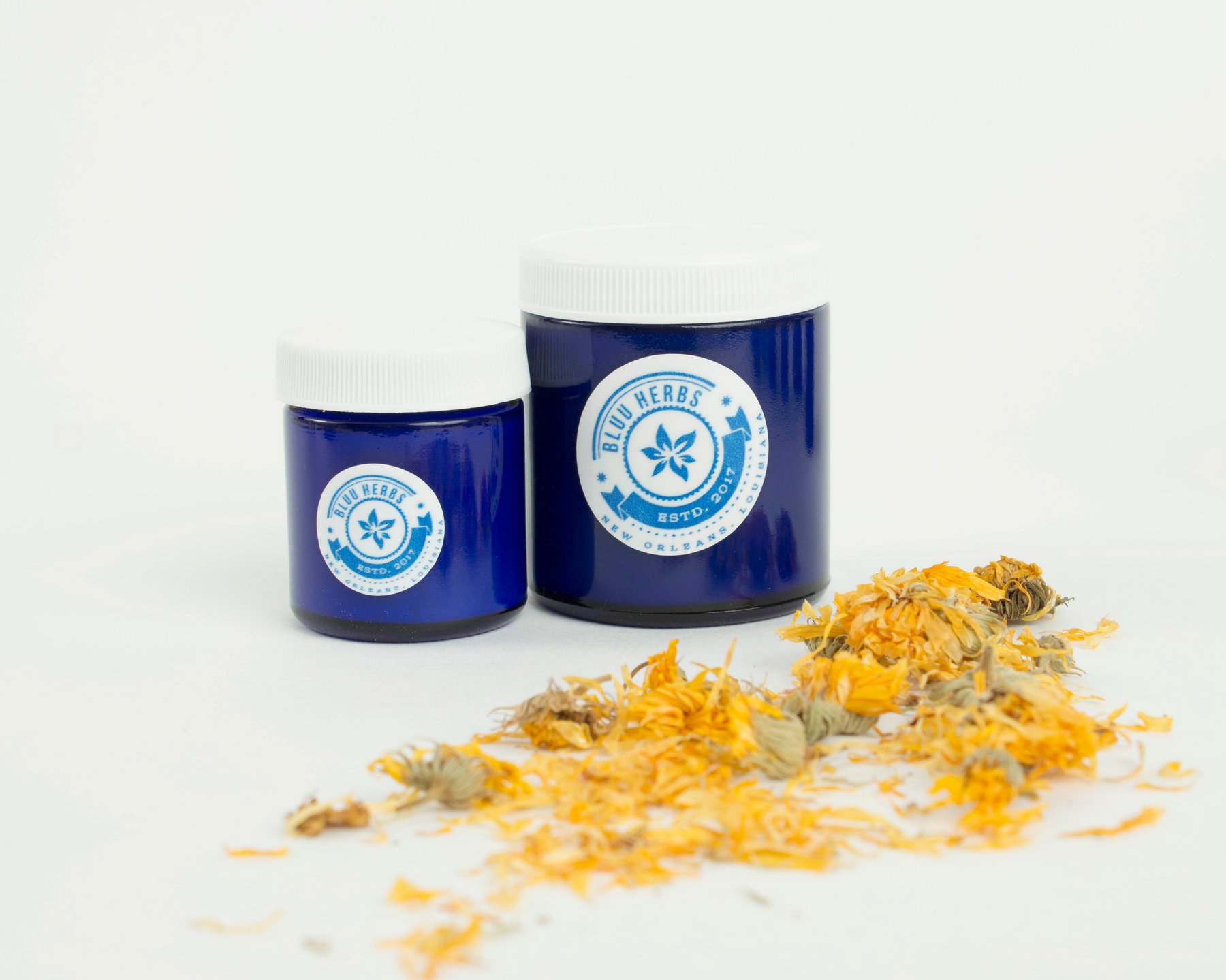Two blue Bluu Herbs jars with dried calendula flowers on a white background