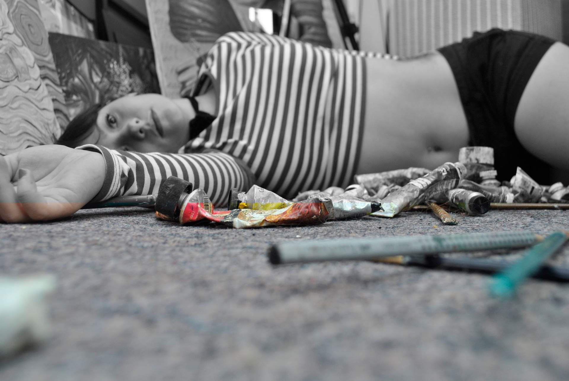 Artist lying among paint tubes and studio materials, rendered mostly in black and white with selective color