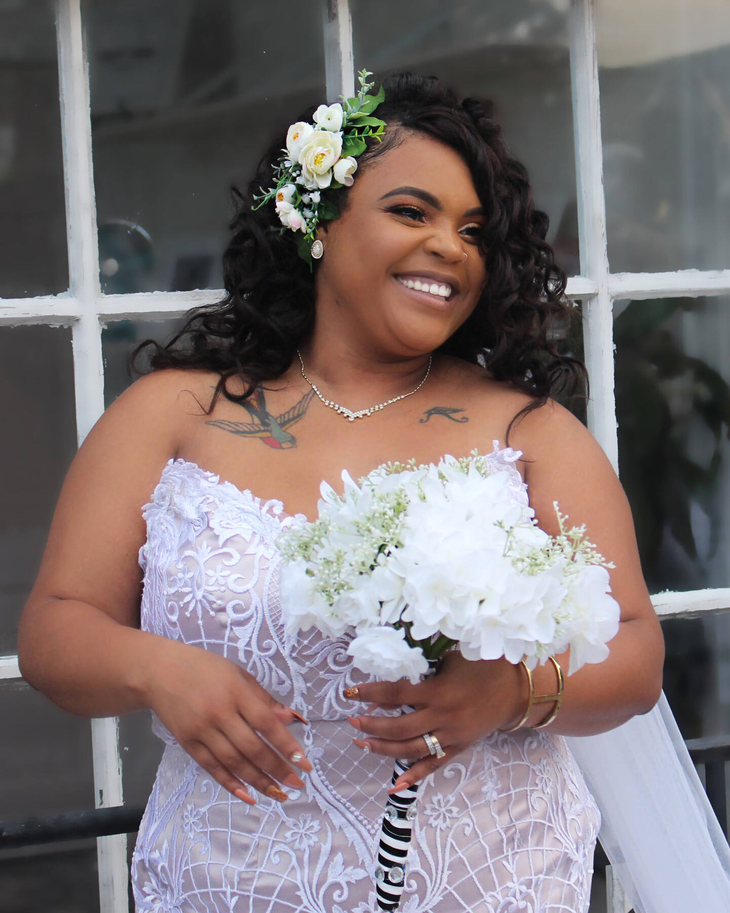 Bride in a lace gown with white flowers in her hair holding a white bouquet