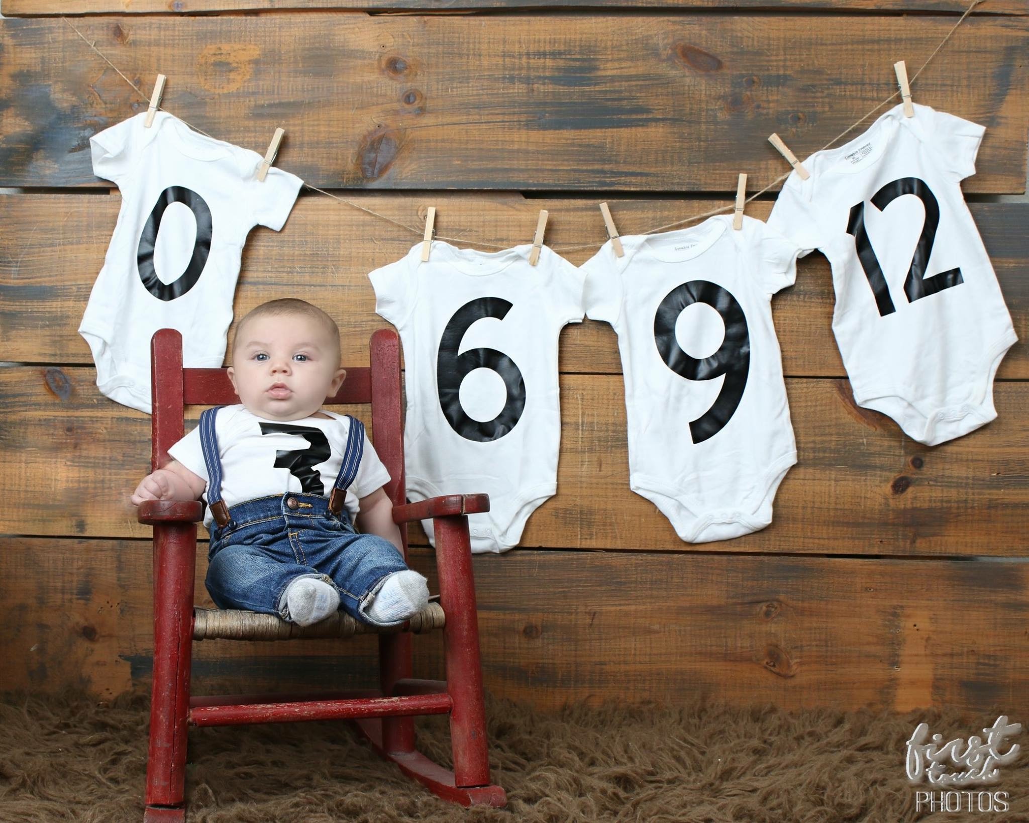 Baby on a red rocking chair beneath onesies lettered 0, 6, 9, and 12
