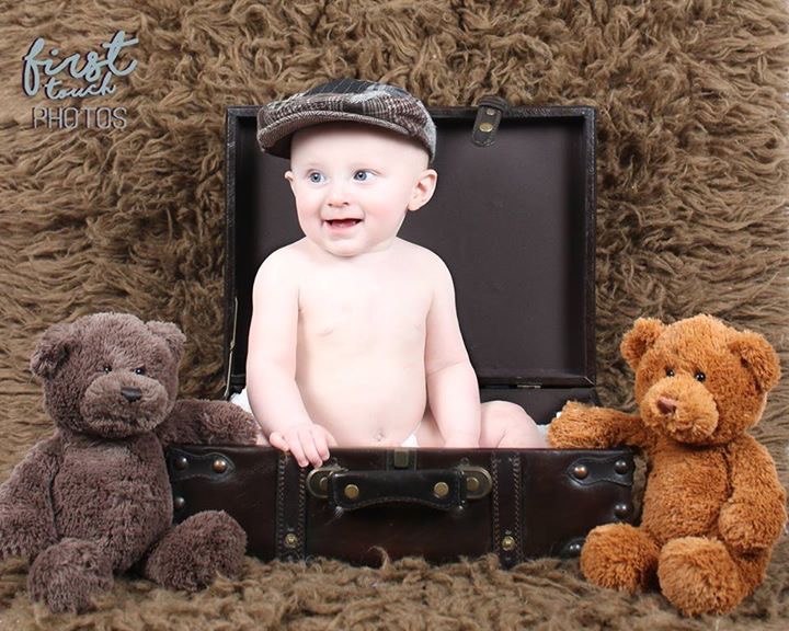 Smiling baby seated in an open suitcase with teddy bears