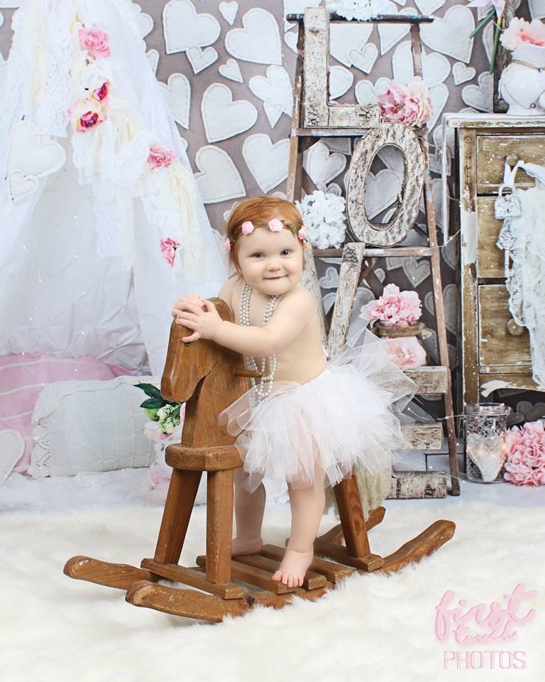 Baby in a white tutu on a wooden rocking horse in front of a LOVE ladder set