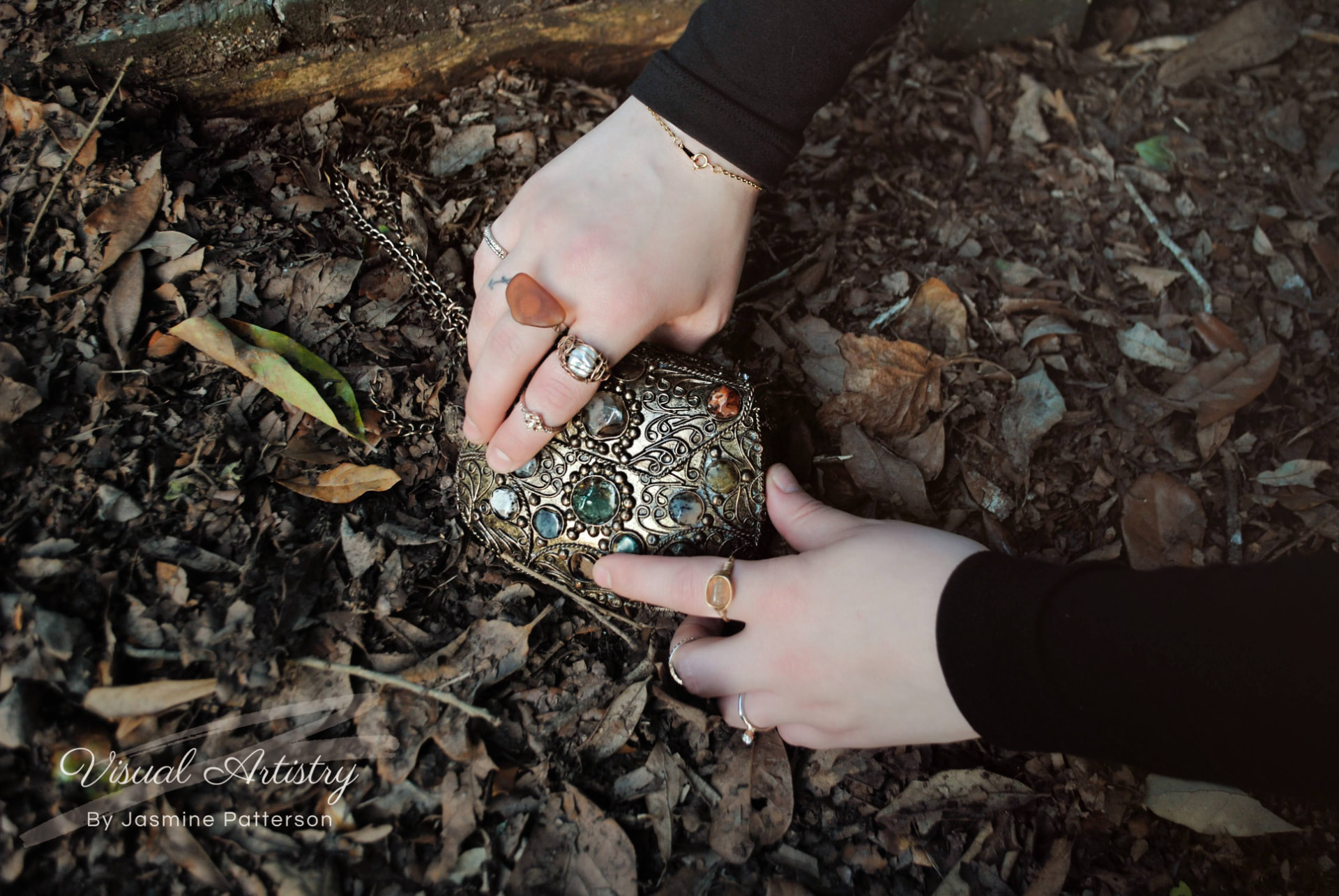 Hands with rings holding an ornate jeweled box on fallen leaves