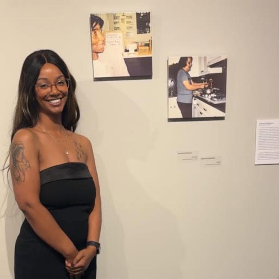 Jasmine Patterson smiling beside her exhibited photographs at the alumni exhibition