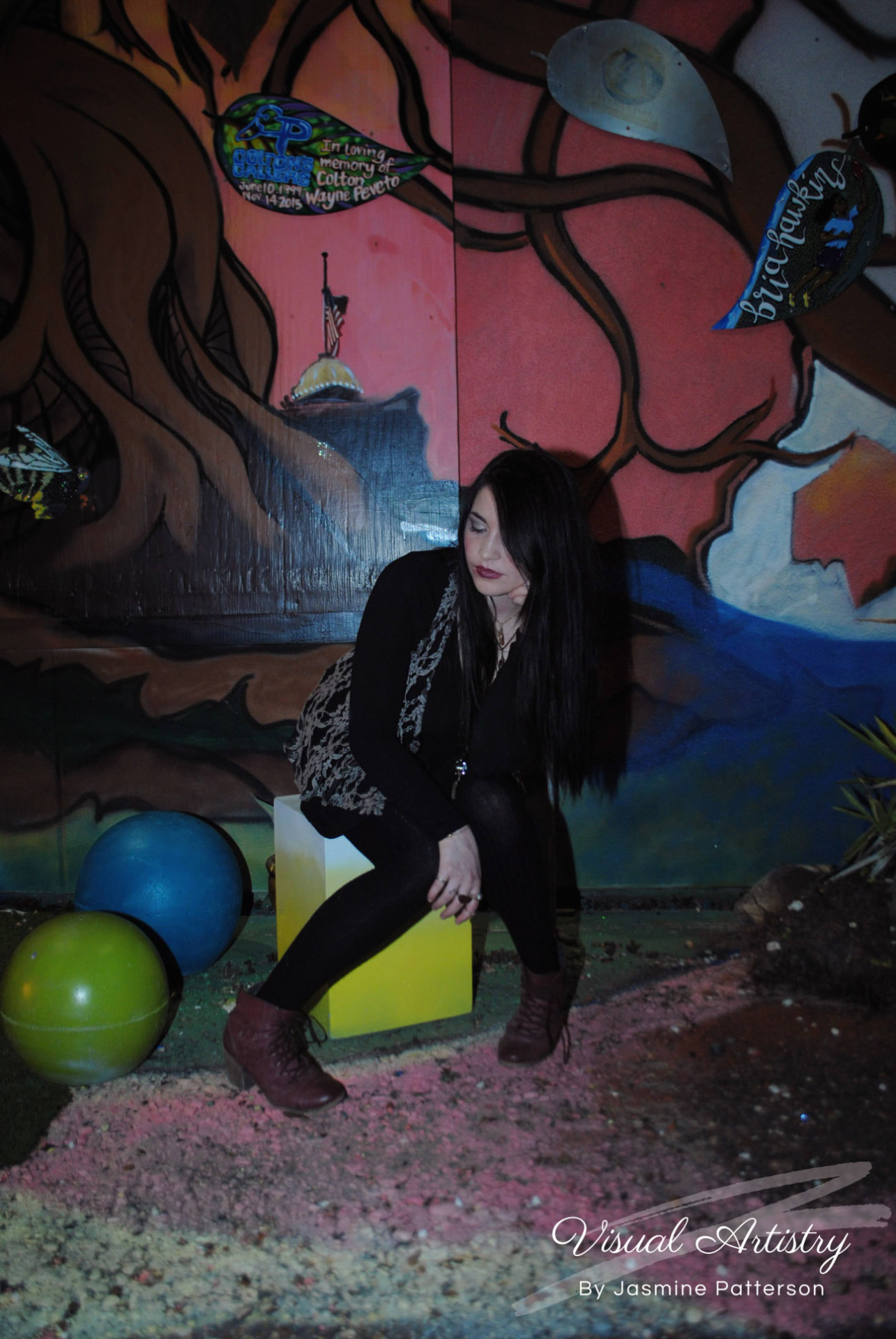 Woman in black and lace seated on a yellow block in front of a painted mural