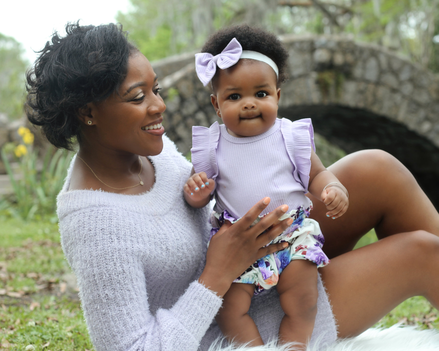 Mother holding her baby daughter in lavender outdoors near a stone bridge