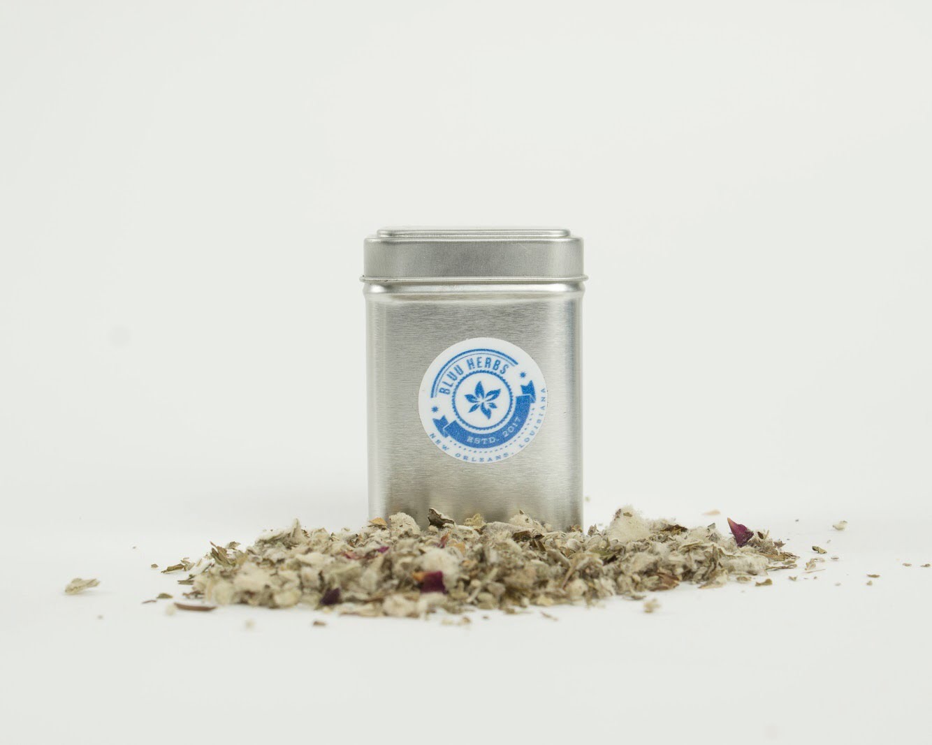 Square silver Bluu Herbs tea tin with loose-leaf tea scattered in front