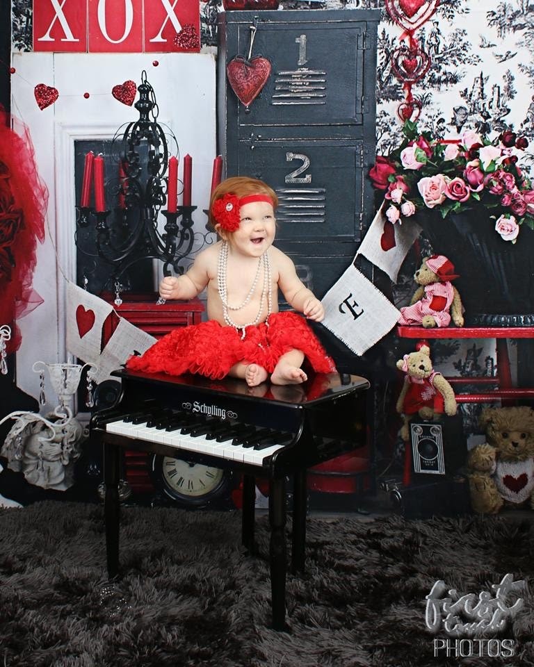 Laughing baby in a red tutu sitting on a toy piano in a Valentine set