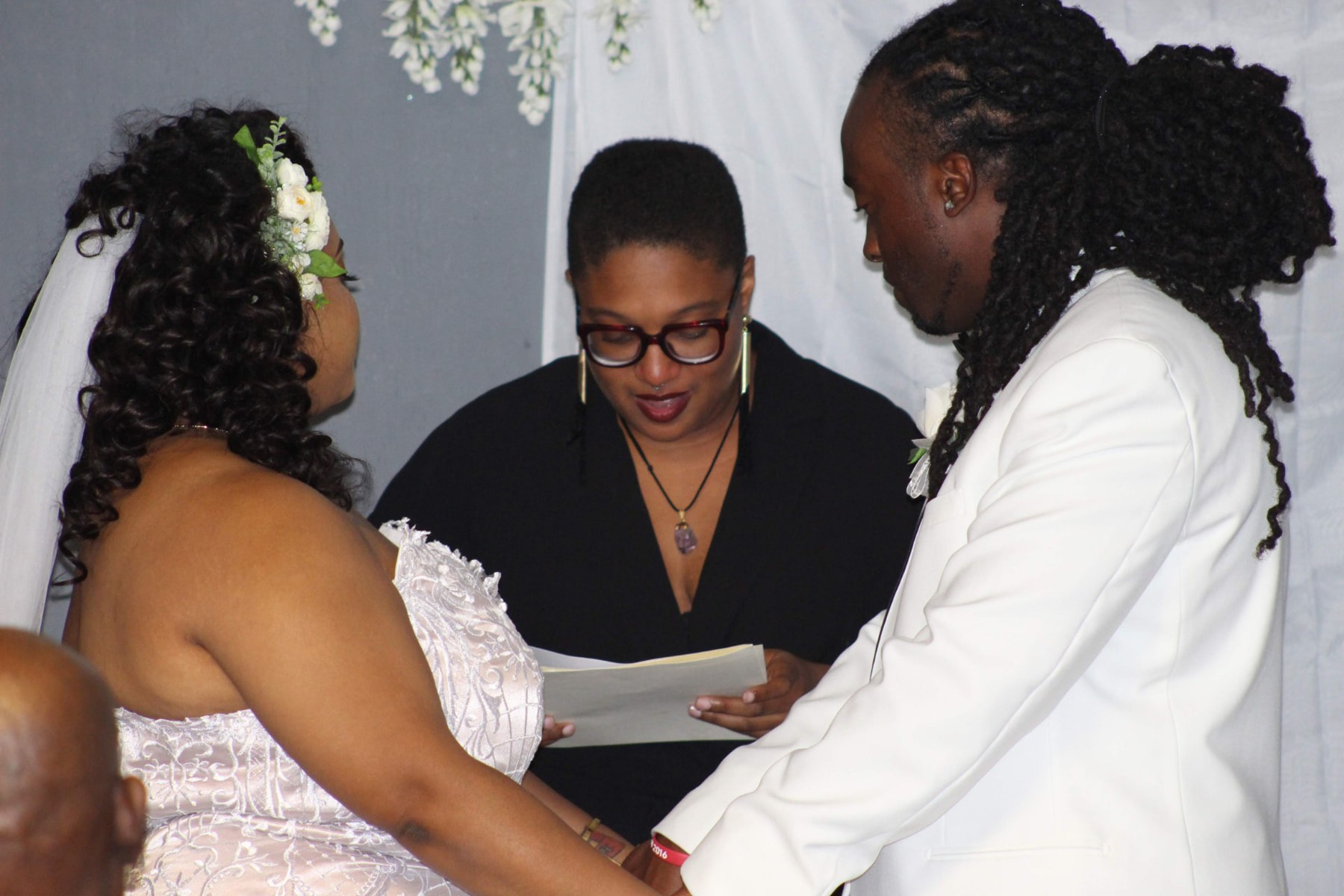 Couple holding hands before the officiant as she reads the vows