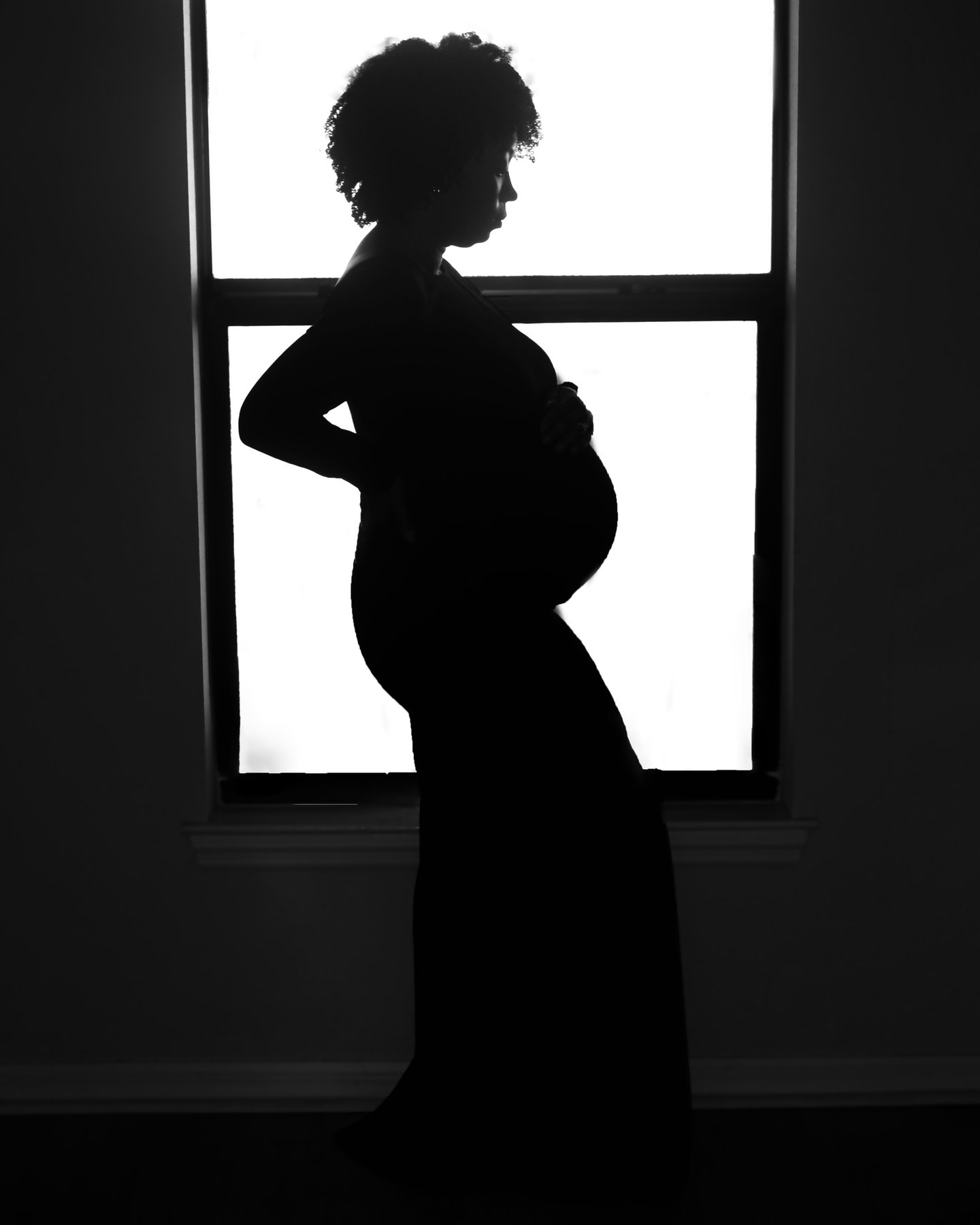 Silhouette of a pregnant woman in profile against a bright window