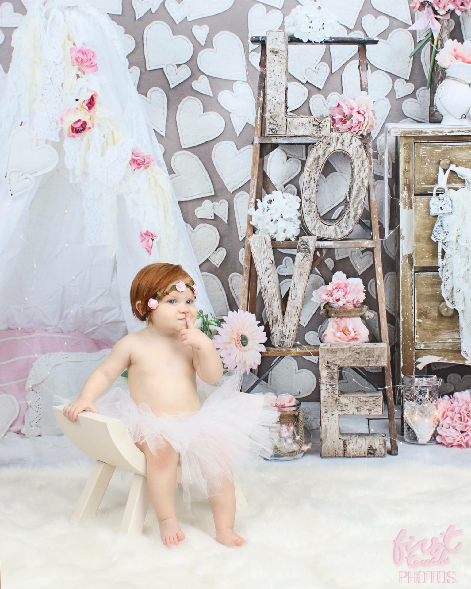 Baby in a pink tutu on a wooden stool in a Valentine set with hearts and LOVE letters