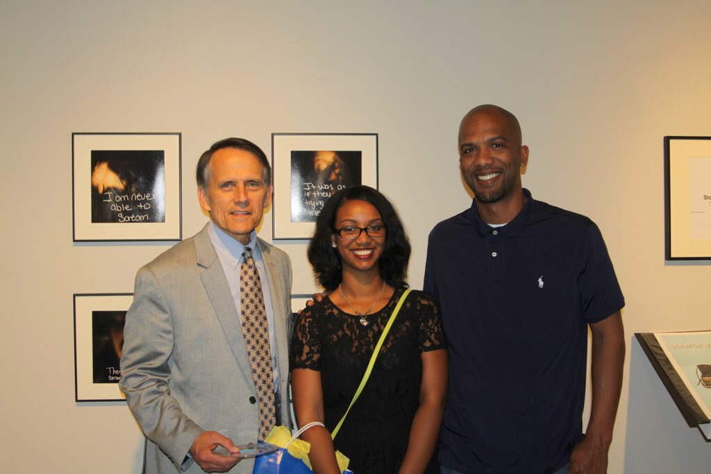 Jasmine Patterson with Mayor Randy Roach and her father in front of framed photographs at her Senior Show Exhibition