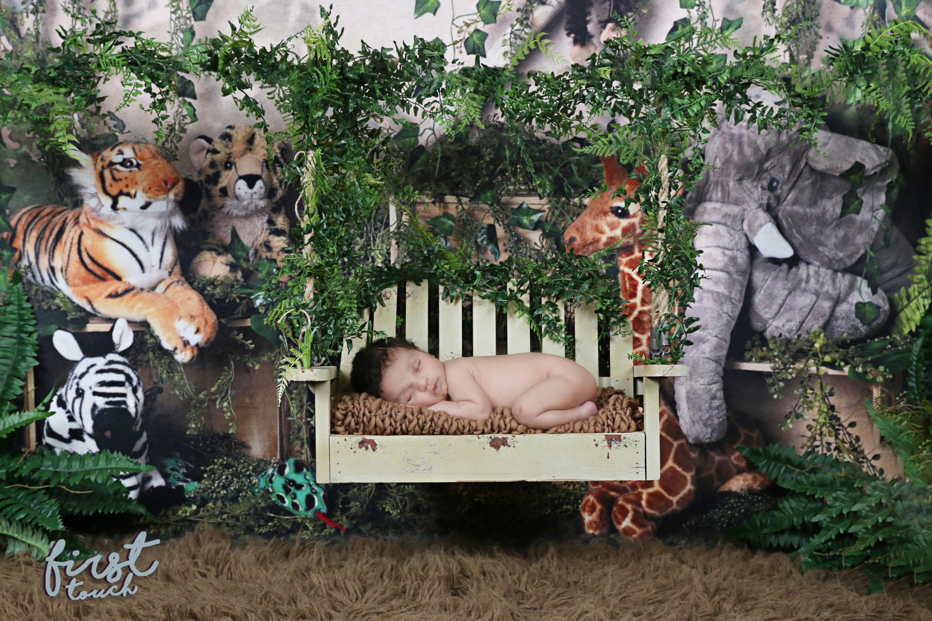 Newborn asleep on a vine-covered swing in a jungle set with plush tiger, giraffe, zebra, and elephant