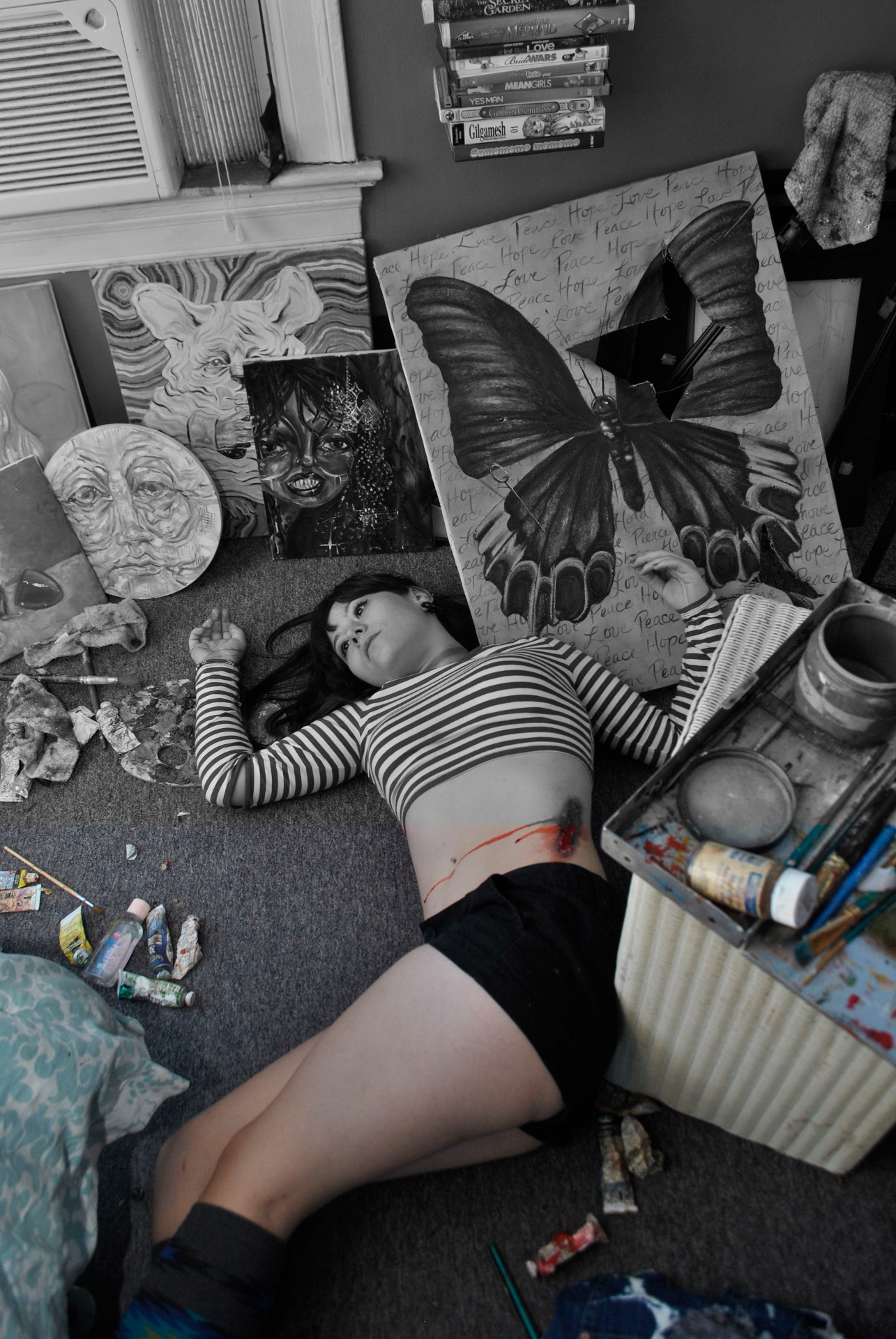 Artist lying among paintings and studio materials, rendered mostly in black and white with selective red color