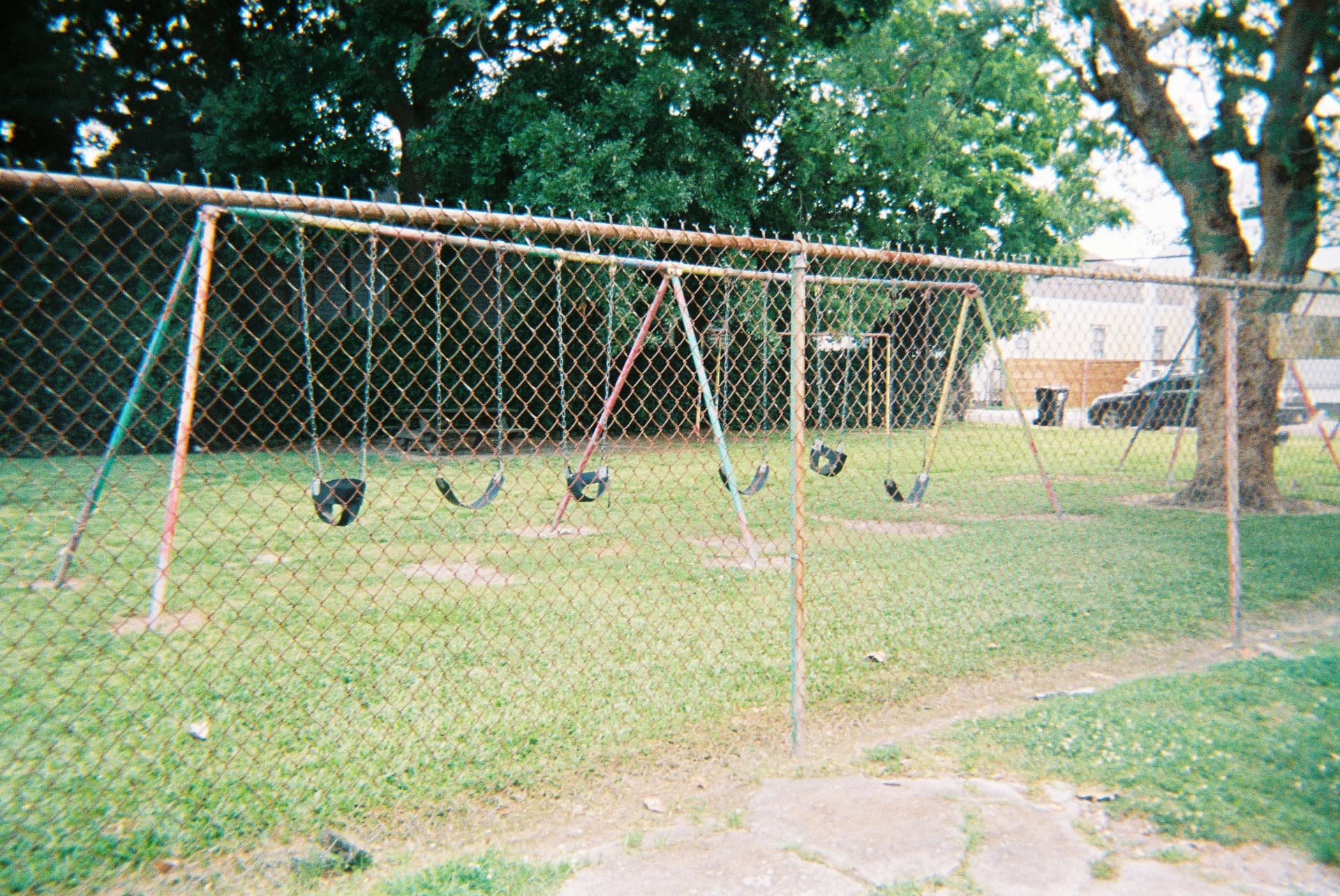Empty swing set behind a rusted chain-link fence