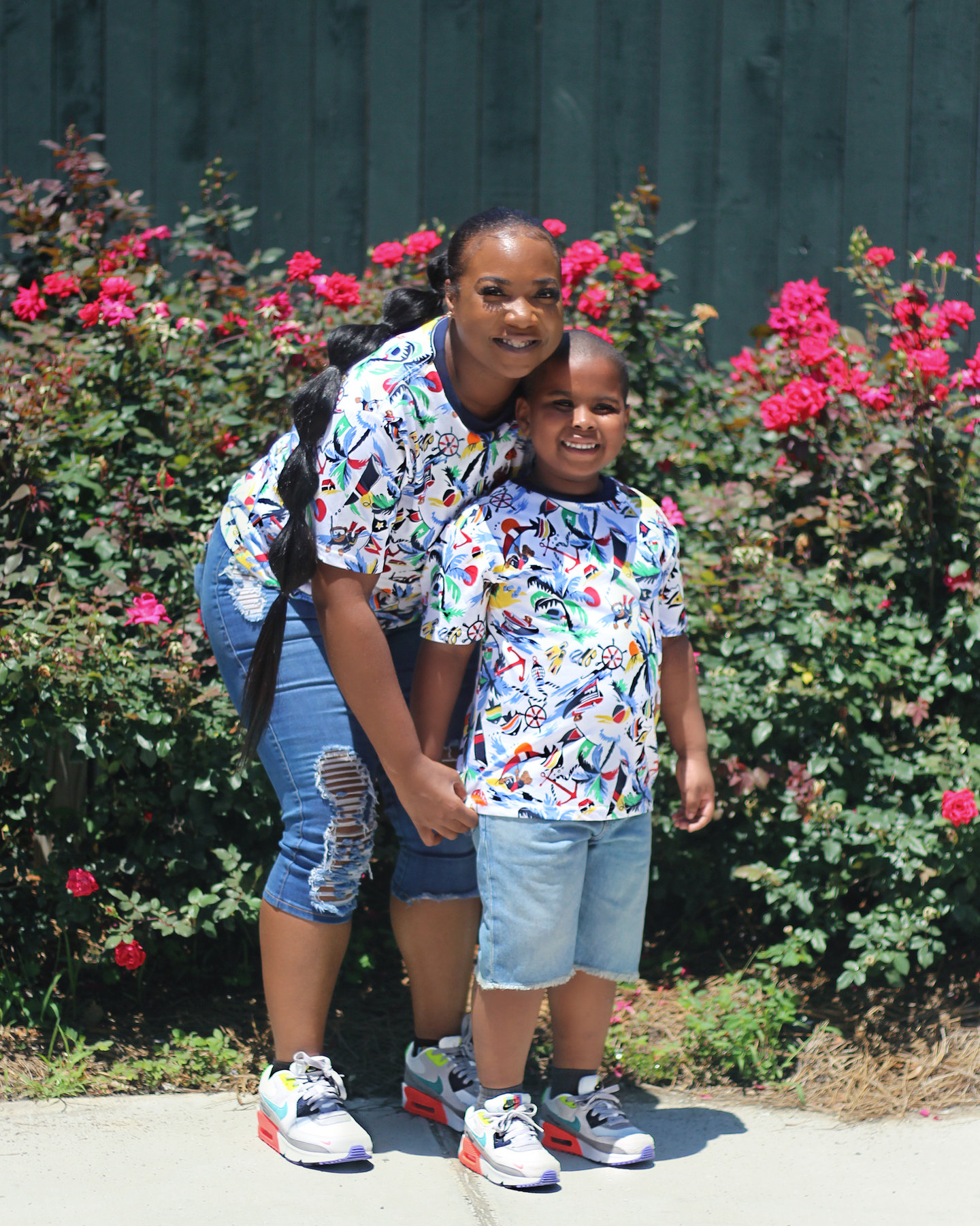 Mother and son in matching patterned shirts standing in front of a rose bush