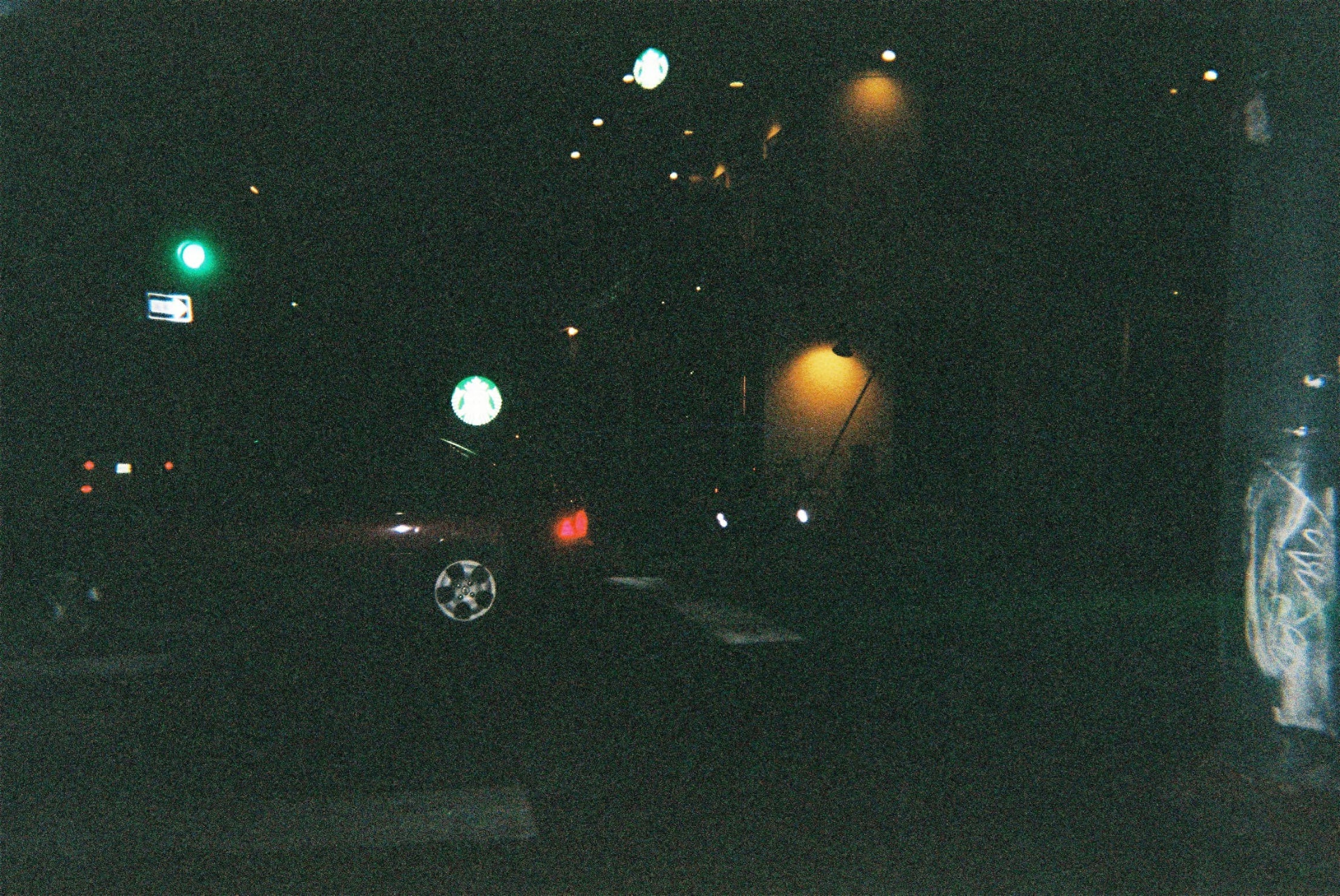 Night street scene on 35mm film with a green traffic light, glowing Starbucks signs, and car tail lights