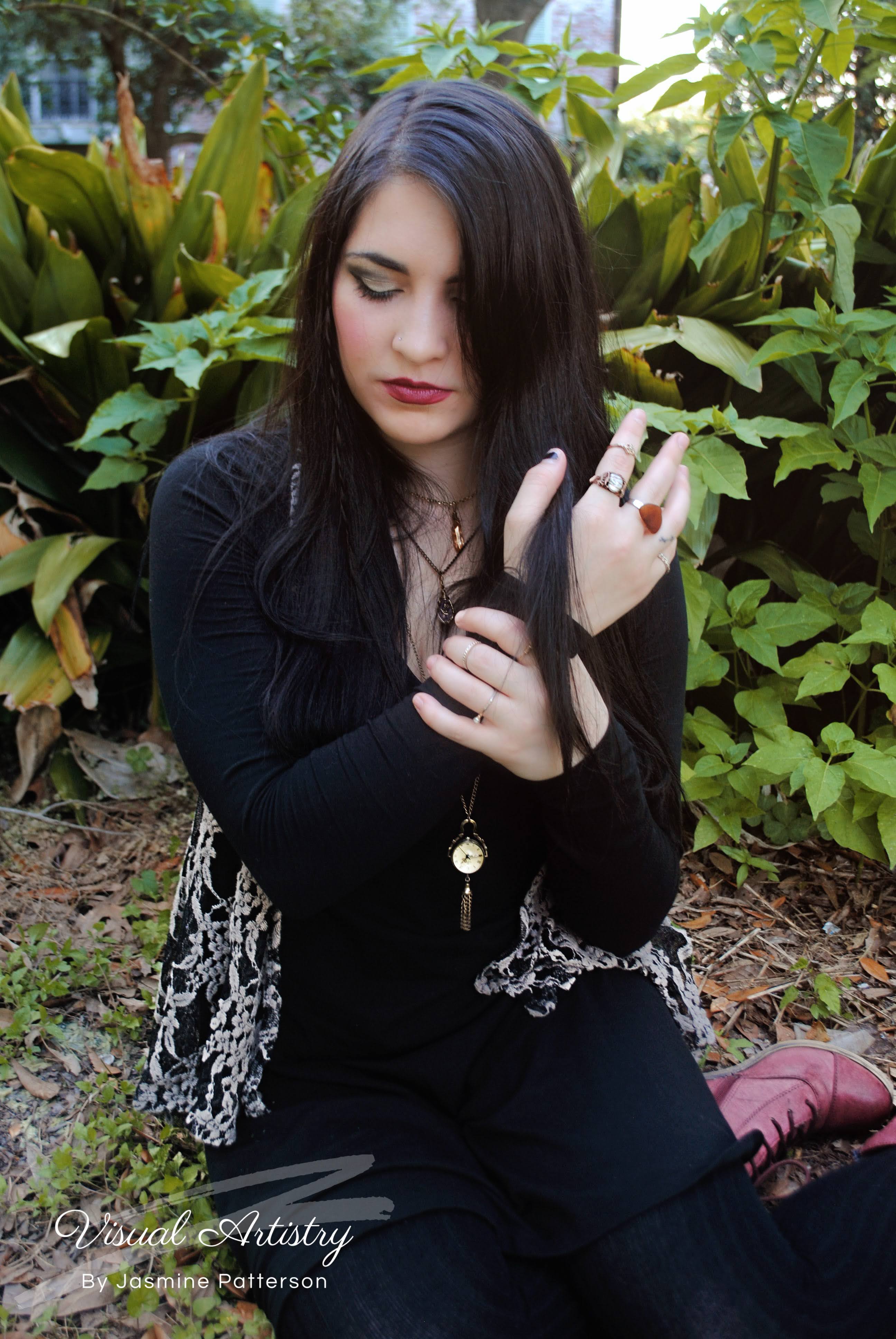 Woman with long dark hair in black seated outdoors among greenery