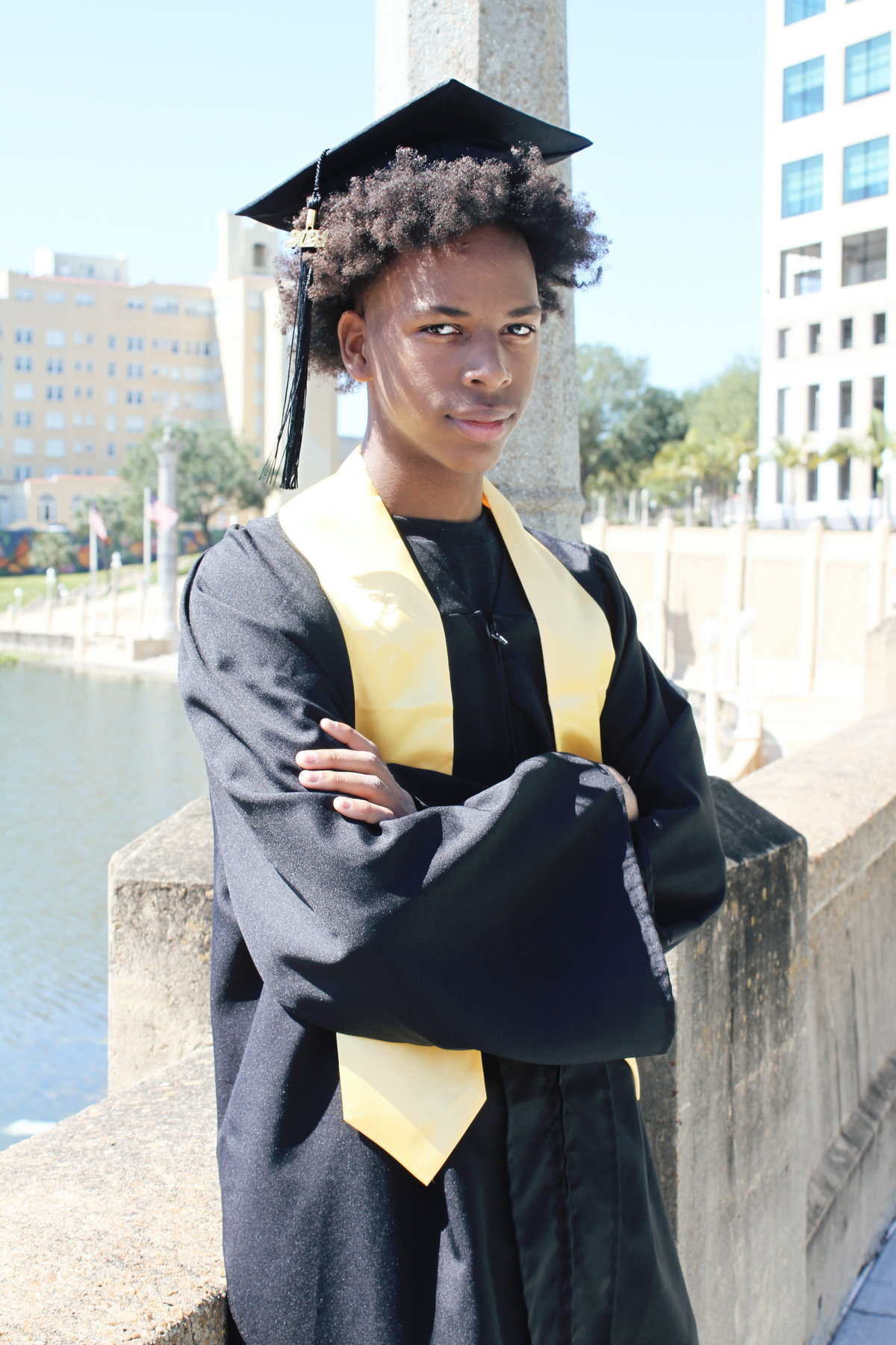 Graduate in cap, gown, and gold stole on a waterfront
