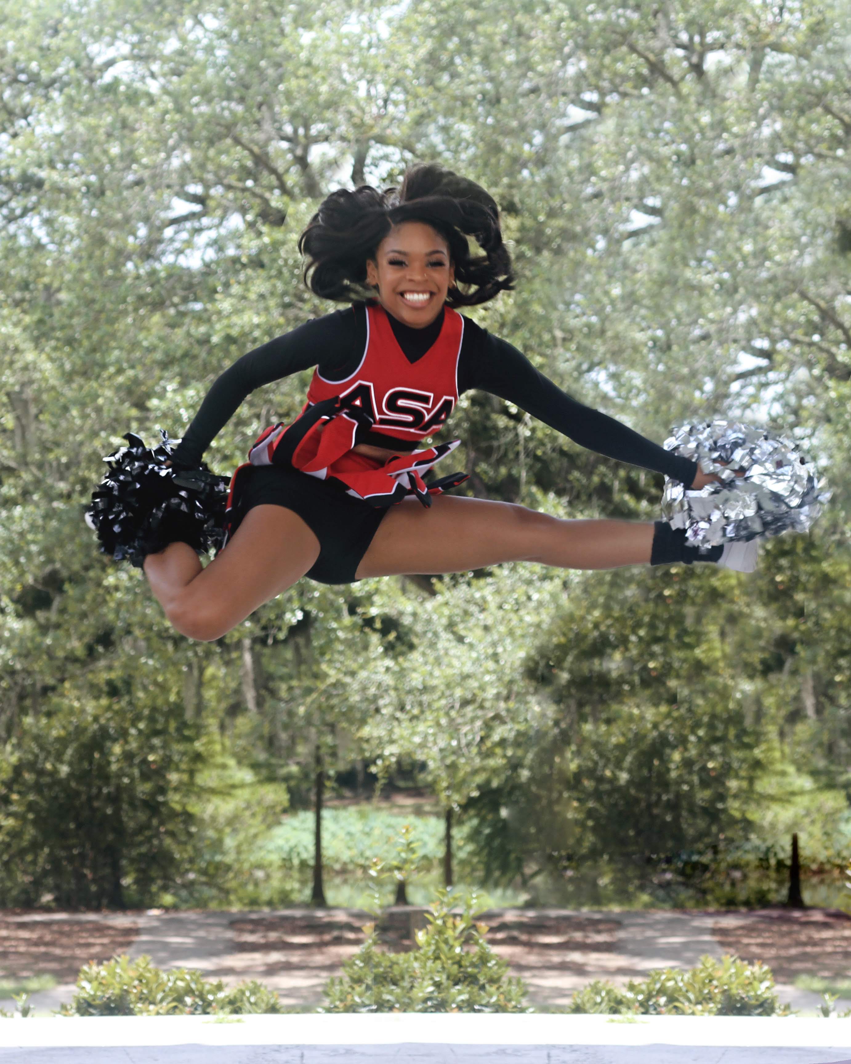 Cheerleader in a red and black uniform performing a jump with pom-poms