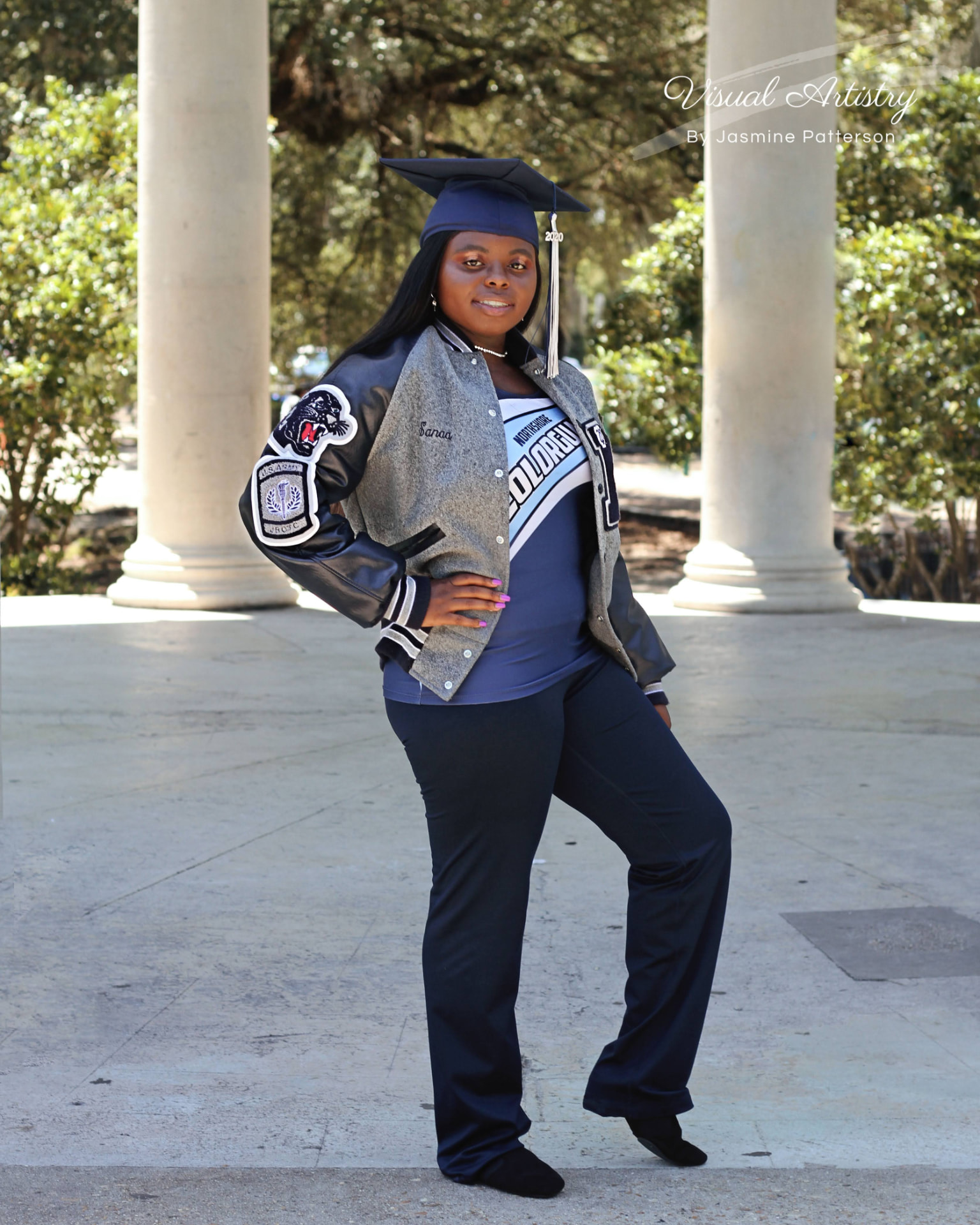 Graduate in a letter jacket and cap standing between white columns