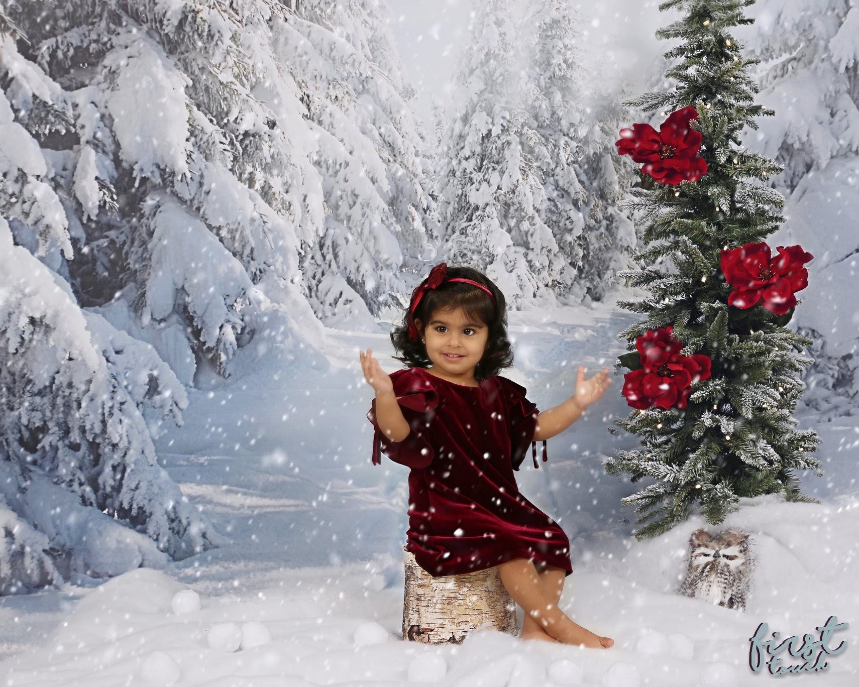 Child in a burgundy dress playing in a snowy holiday set