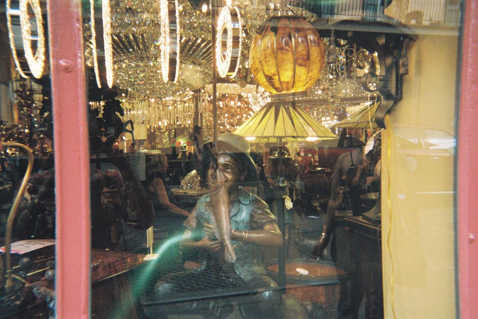 Antique shop window filled with chandeliers, lamps, and figurines reflected in the glass
