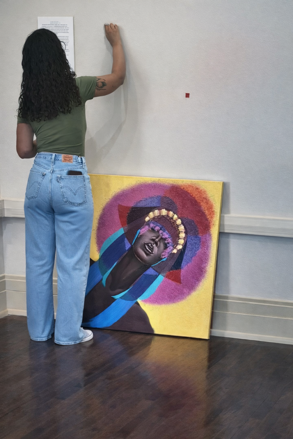 Jasmine Patterson marking placement on a gallery wall beside a colorful portrait artwork