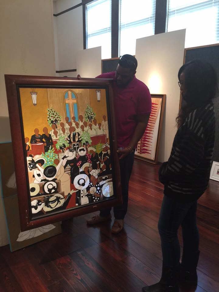 Jasmine Patterson helping an artist handle a framed artwork inside Black Heritage Gallery