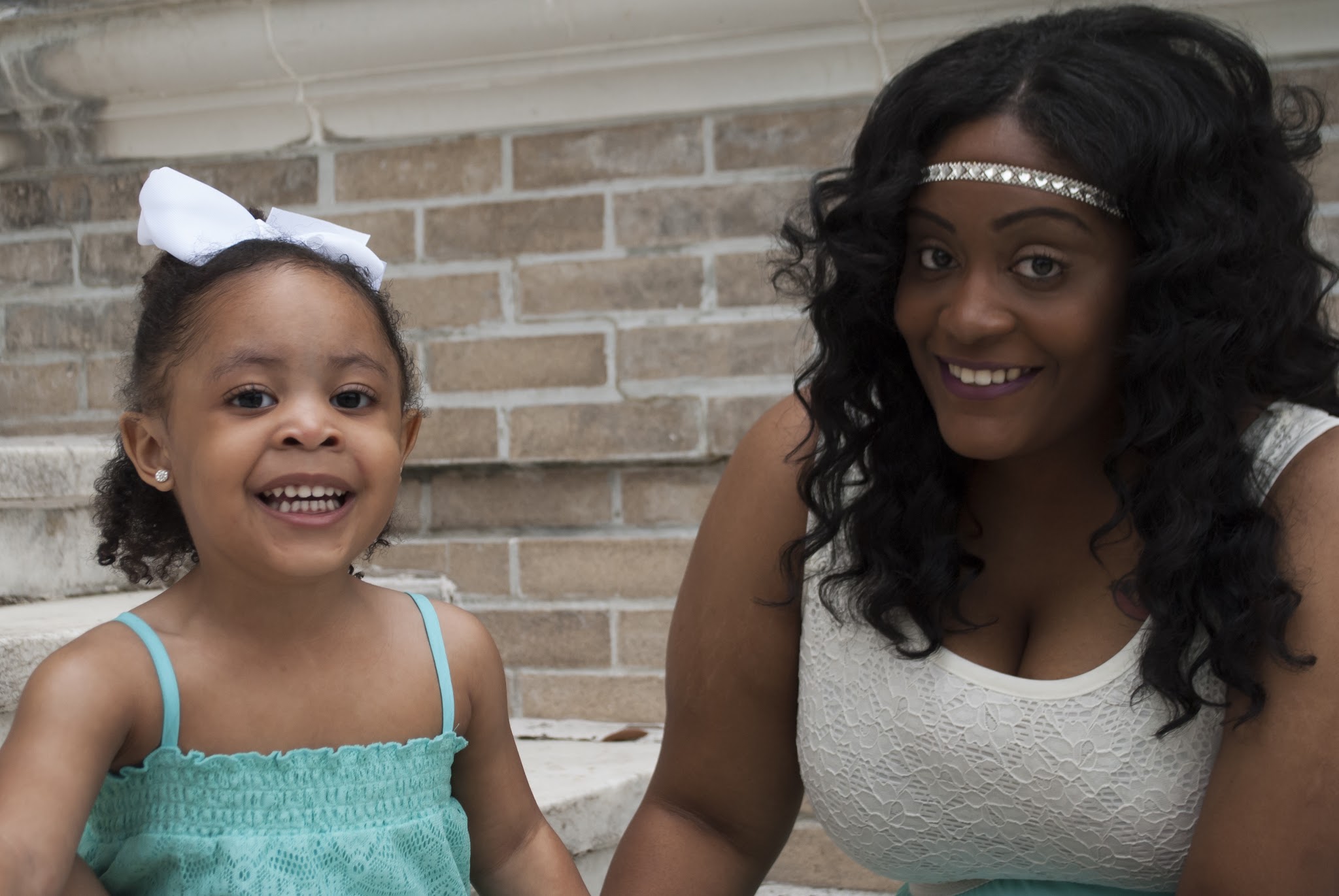 Mother and daughter smiling together outdoors, the daughter in a mint dress and white bow