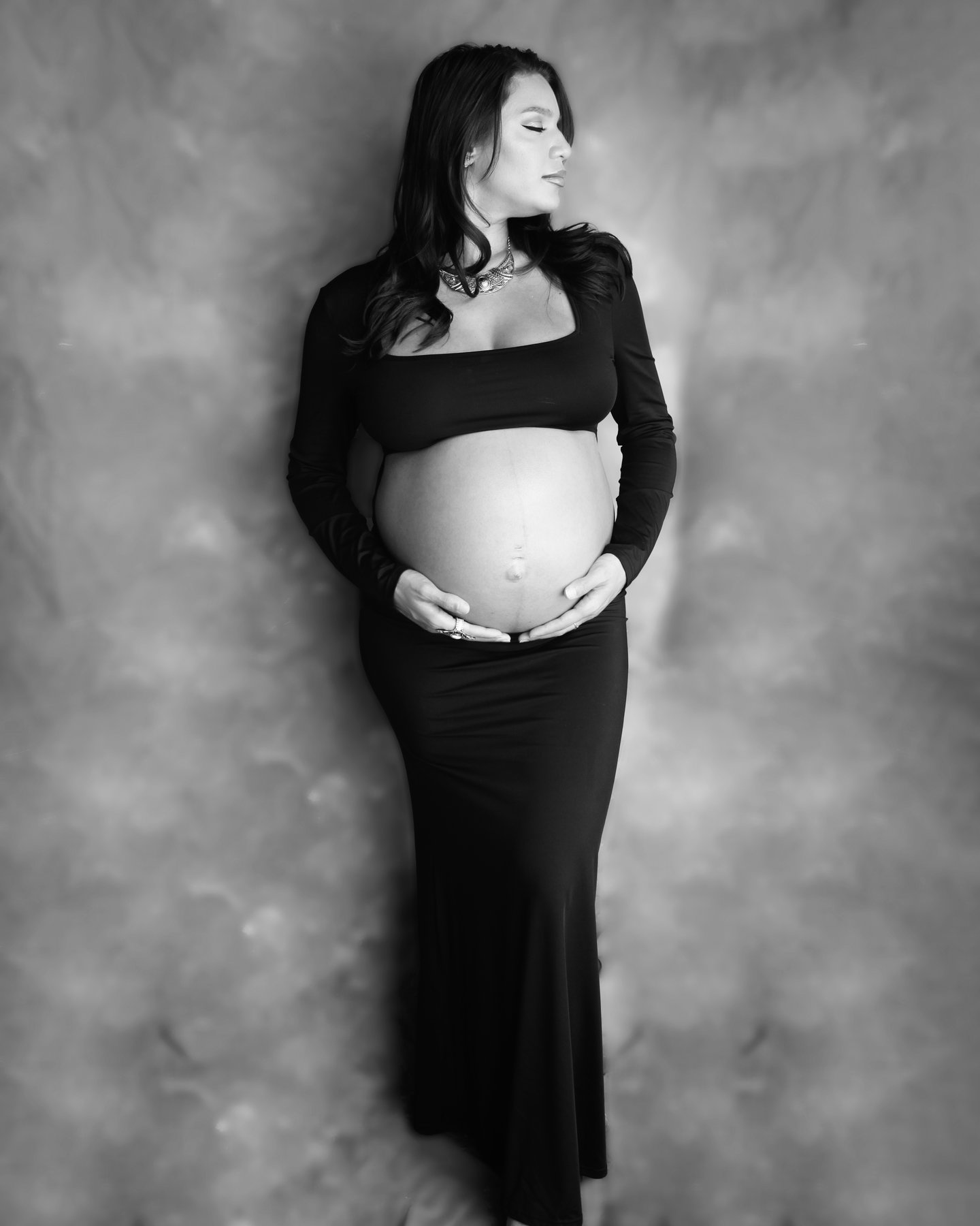 Black-and-white studio maternity portrait of a woman in a long skirt