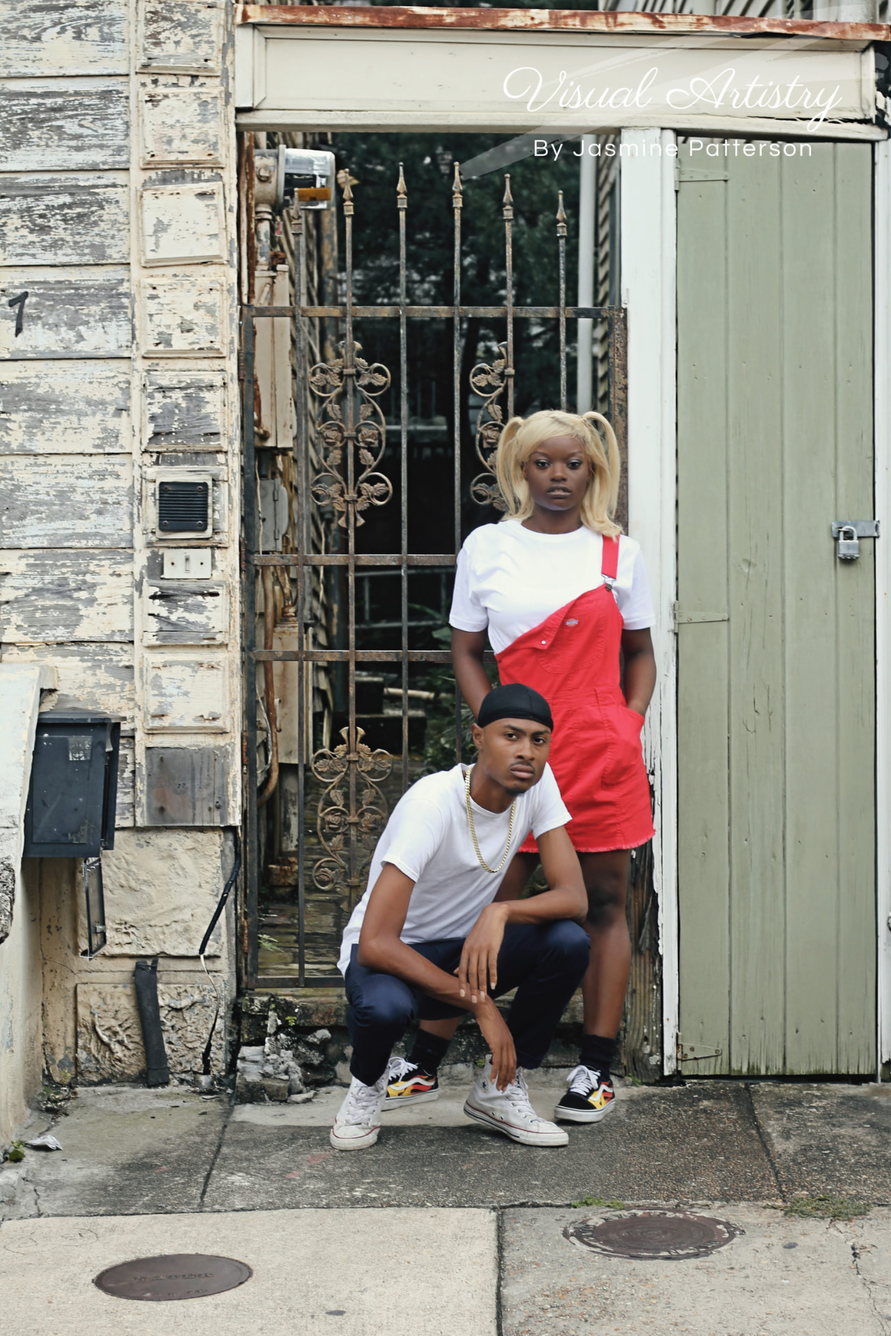 Two models at an iron gate, the young woman standing and the young man crouching