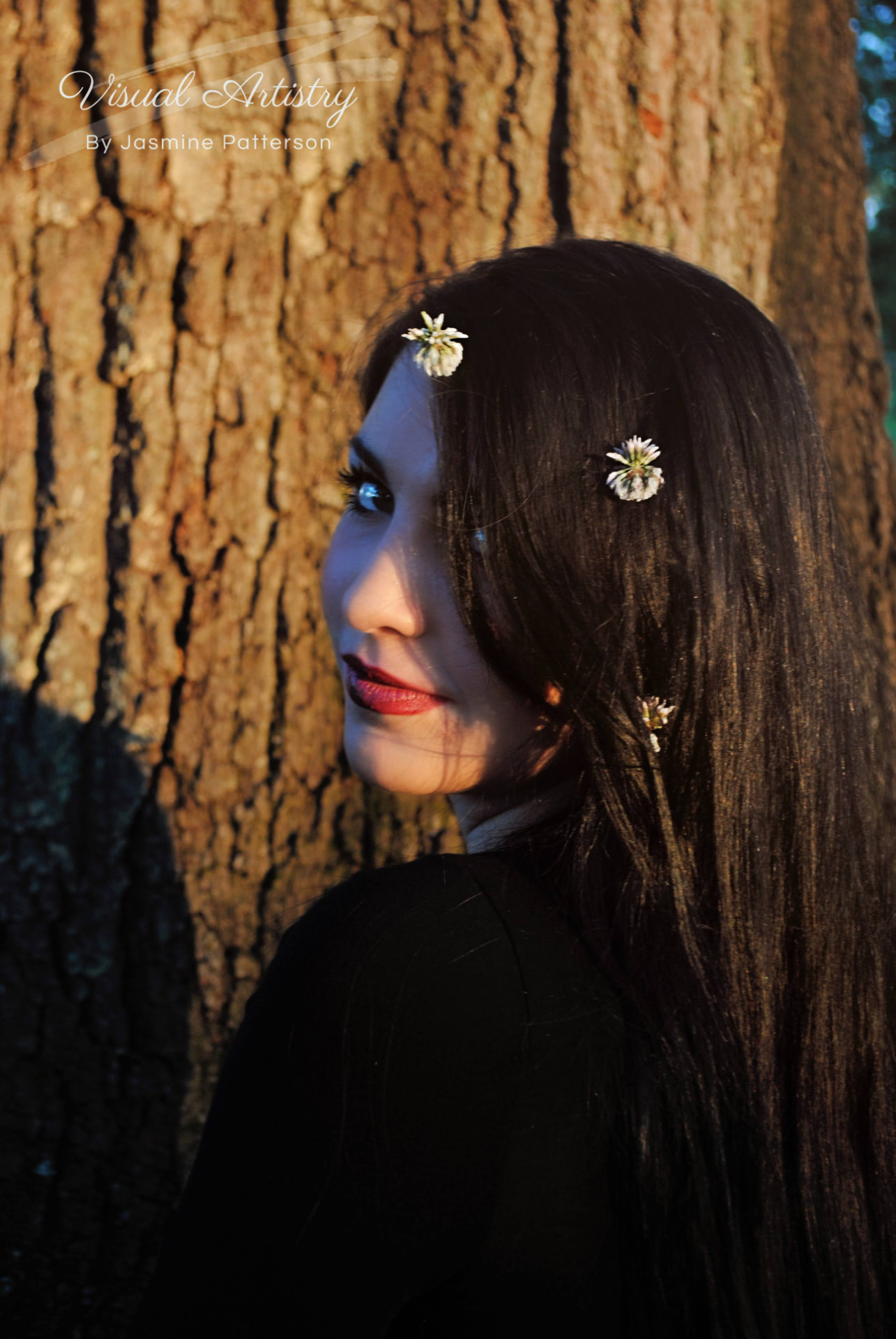 Dark-haired woman with flowers in her hair looking over her shoulder against an oak trunk