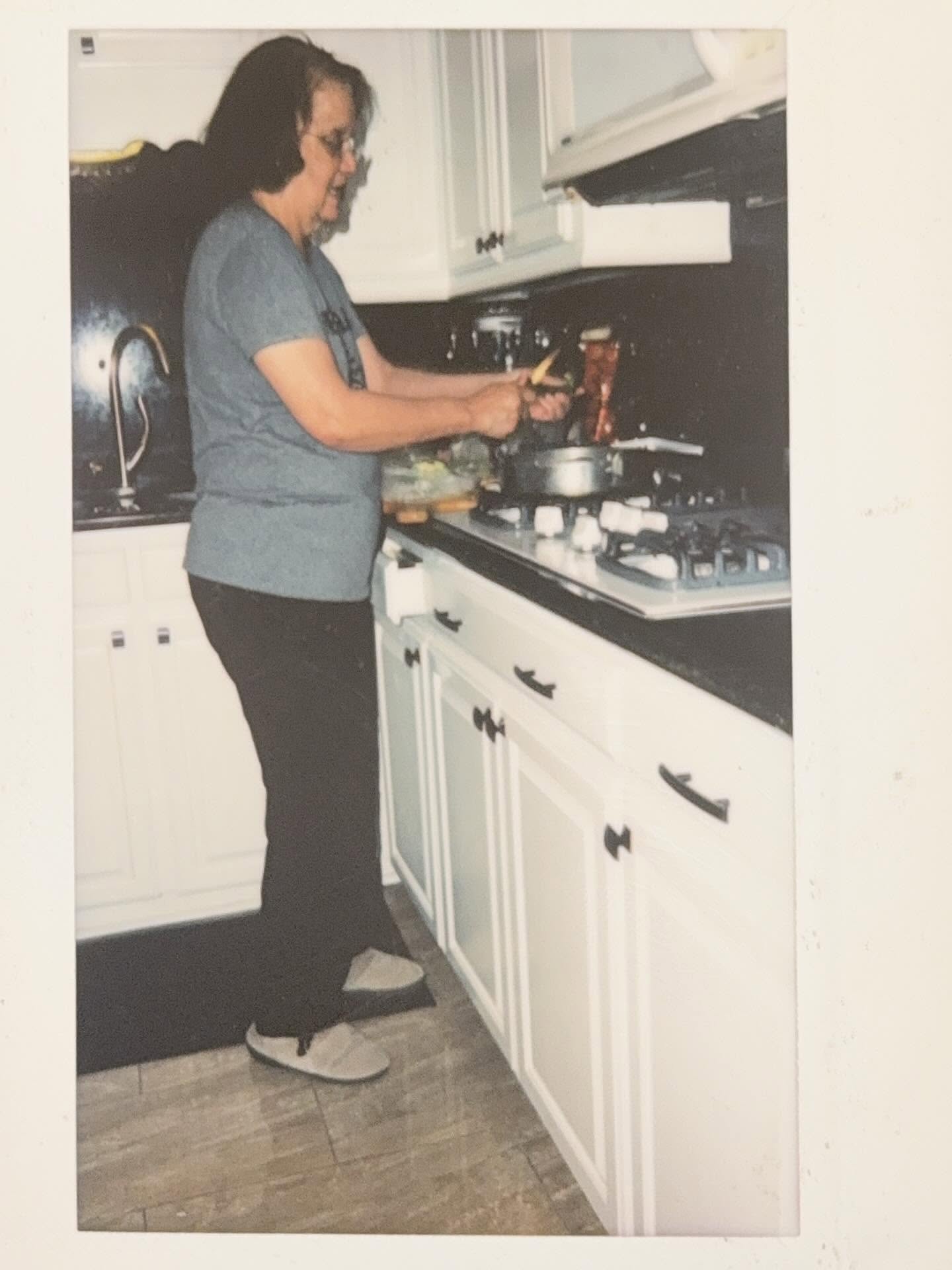 Exhibited photograph of a woman cooking at a stove in a home kitchen