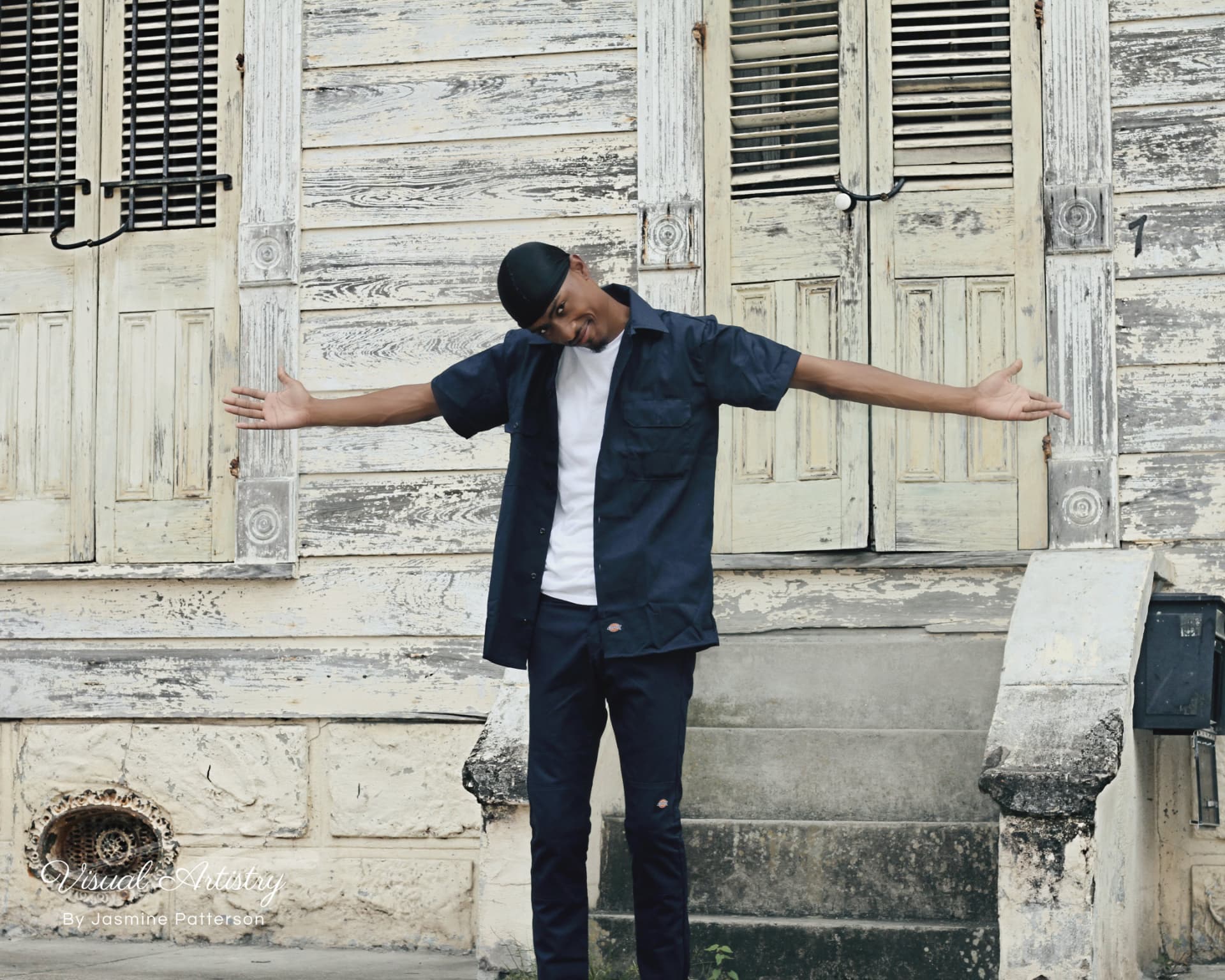 Young man standing with arms spread in front of weathered cottage doors