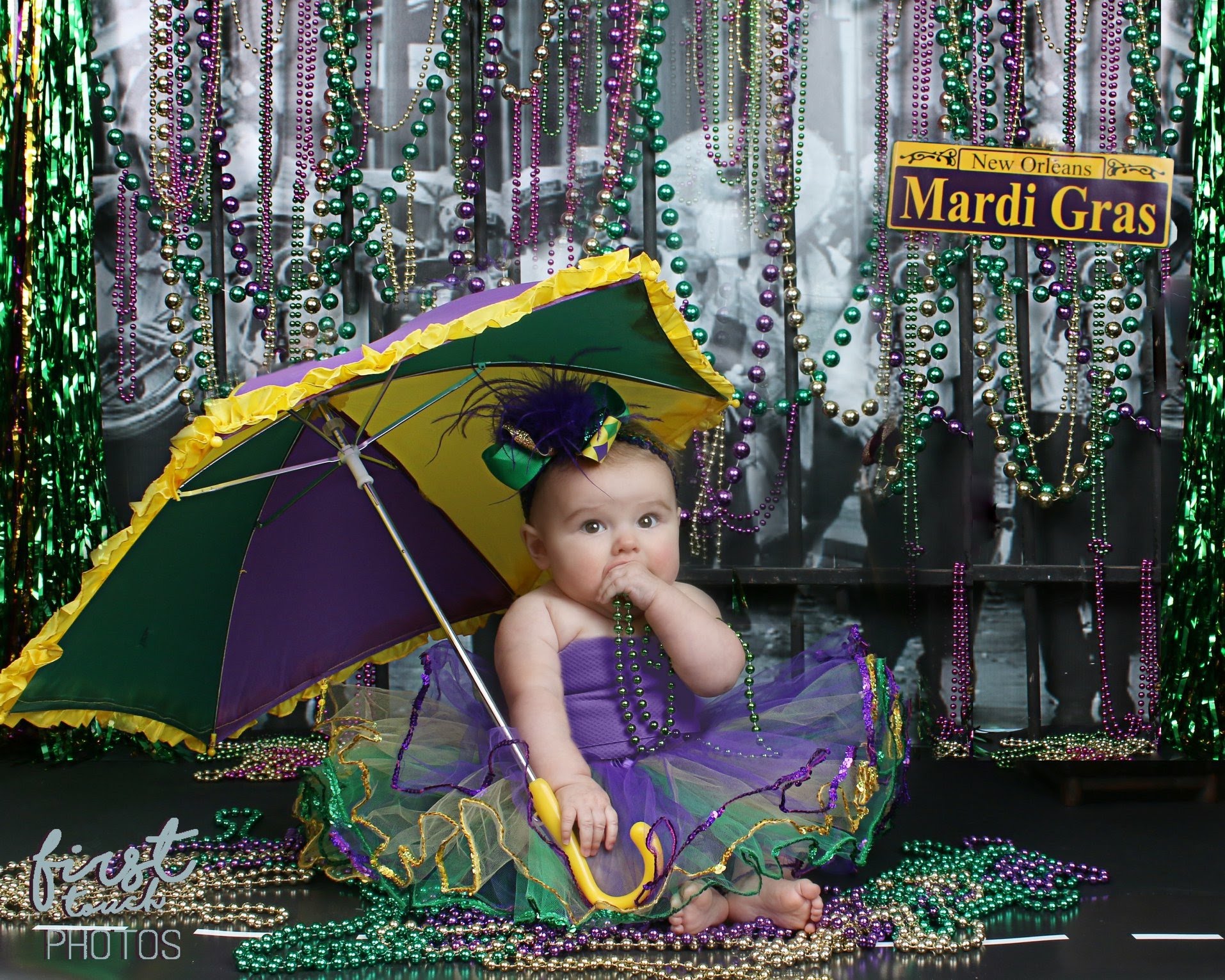 Baby in a purple and green tutu under a Mardi Gras umbrella surrounded by beads