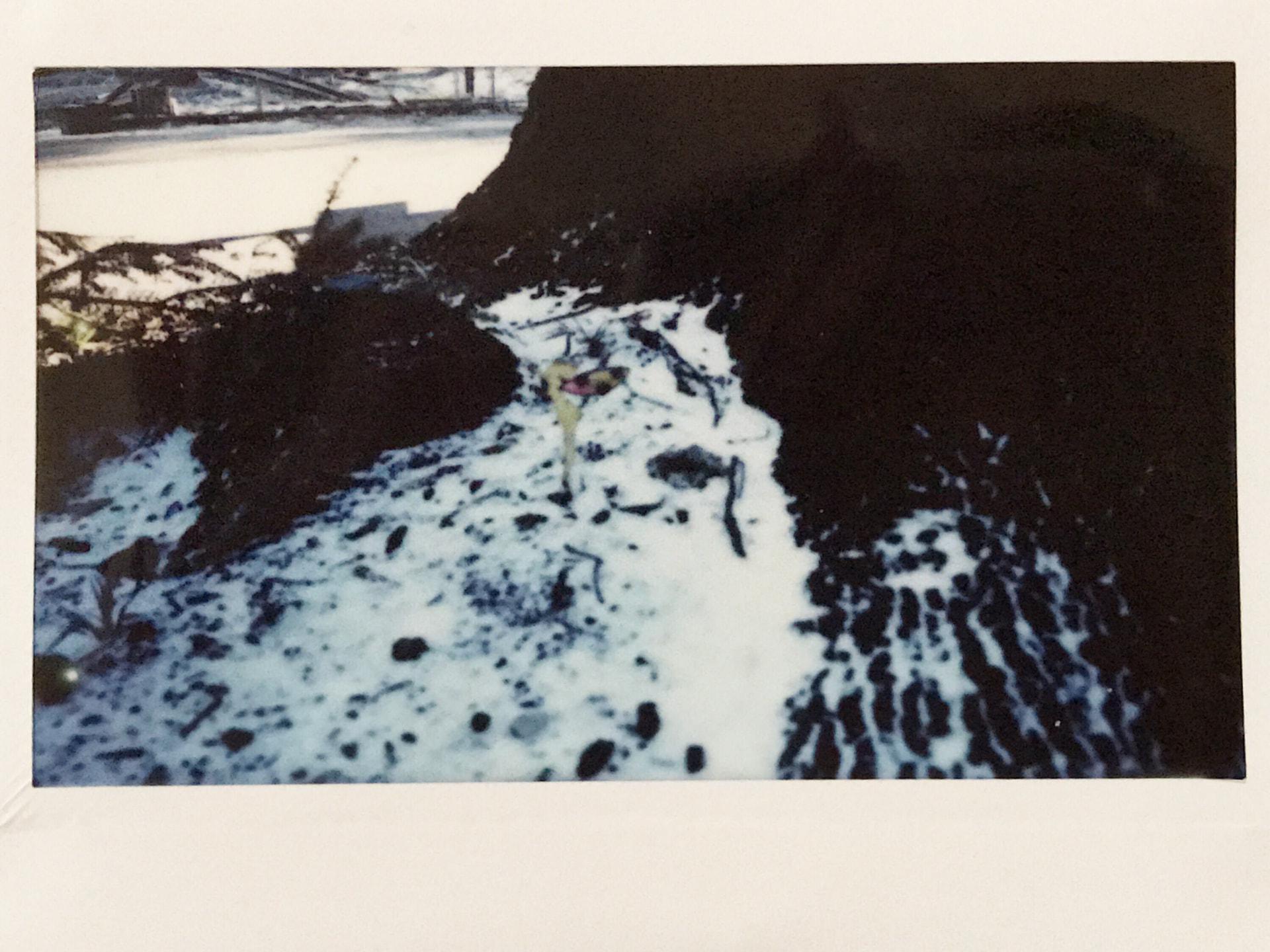 Instant film photo of snow piled along a dark wall