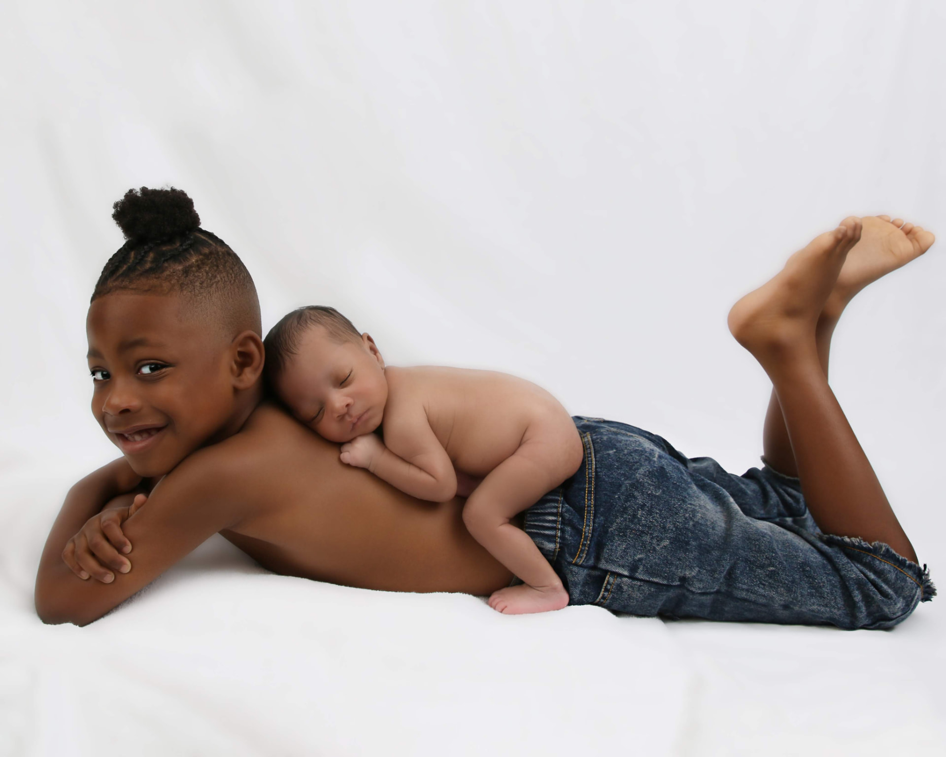 Big brother lying beside his newborn sibling on a white studio blanket