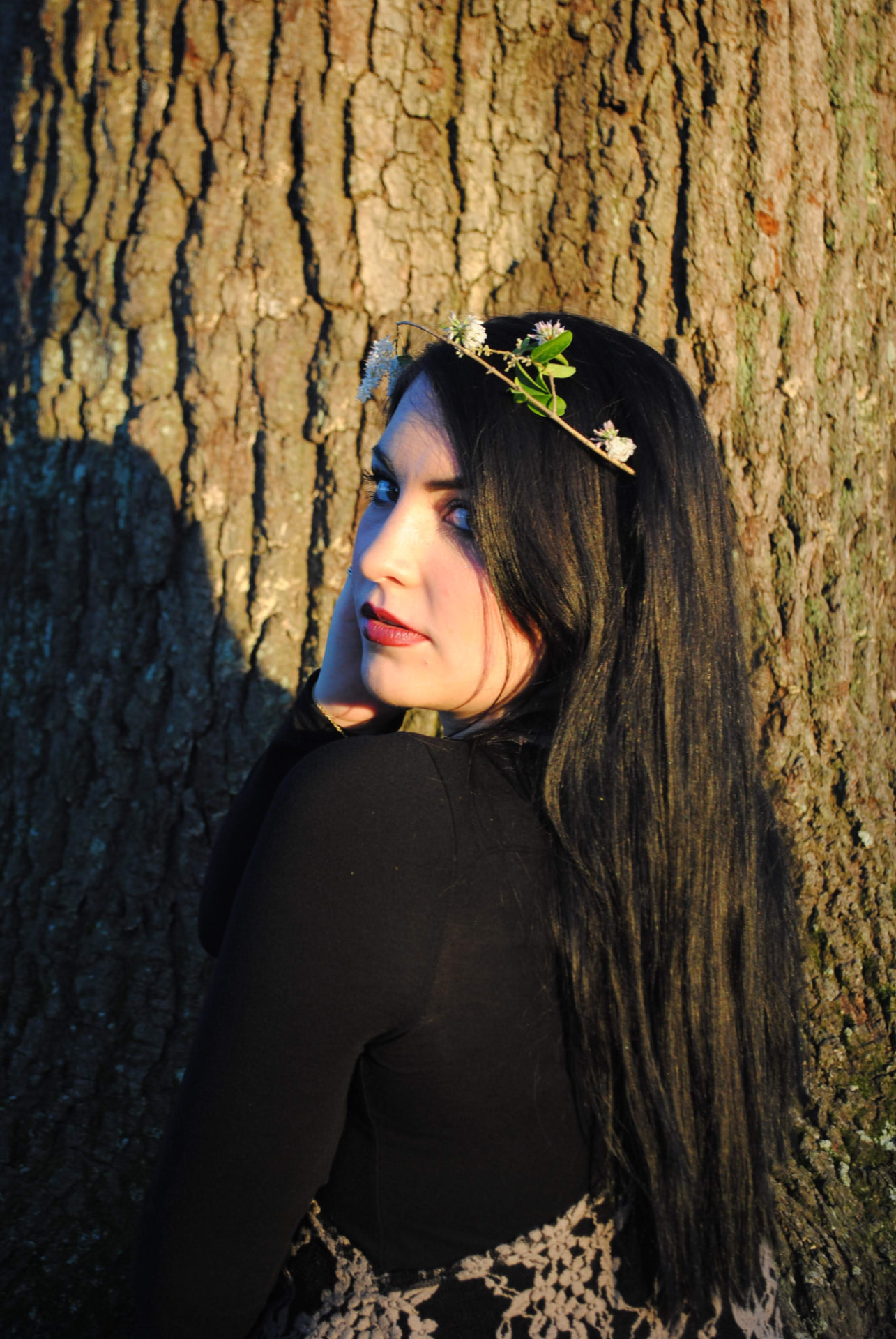 Woman with a flower crown looking over her shoulder against an oak trunk in warm light