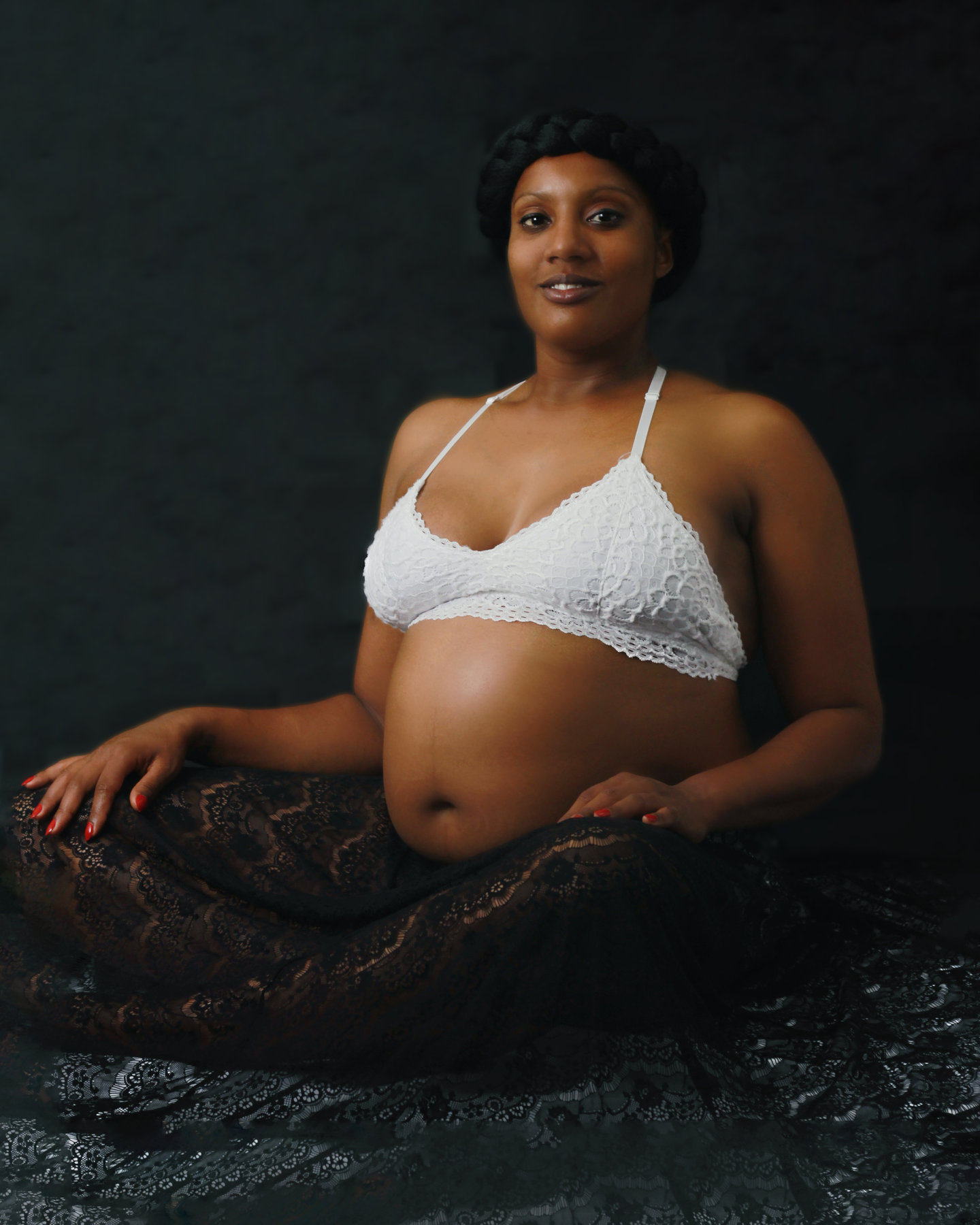 Pregnant woman in a white top seated against a dark studio backdrop
