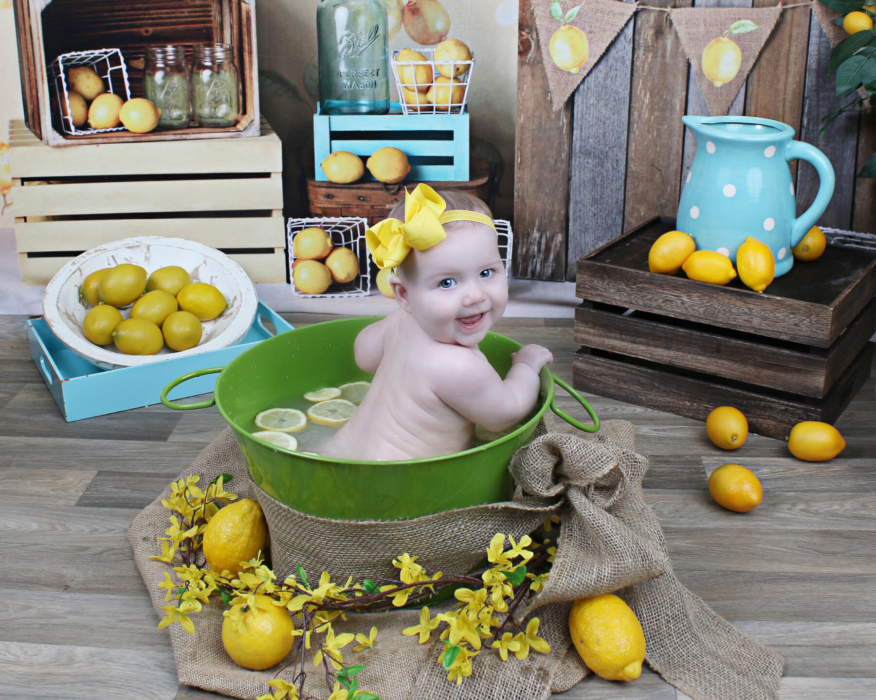Smiling baby in a green tub set with lemons, crates, and a blue pitcher